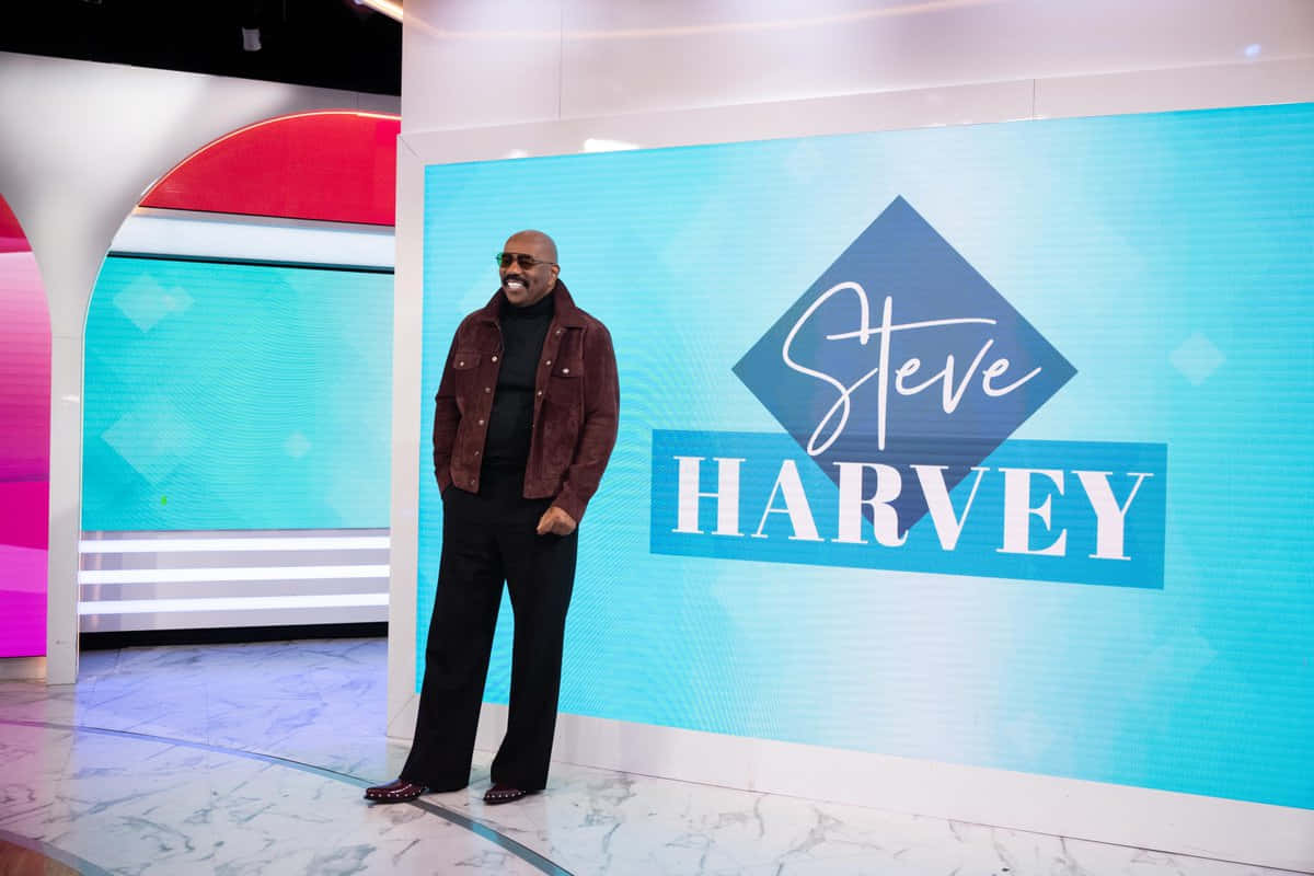 Steve Harvey 在工作室微笑，身後藍色屏幕上顯示他的名字。