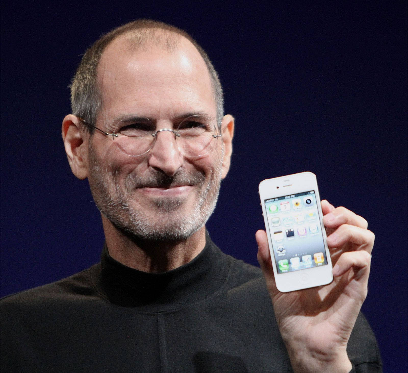 Steve Jobs 在舞台上帶著溫暖的笑容手持 iPhone。