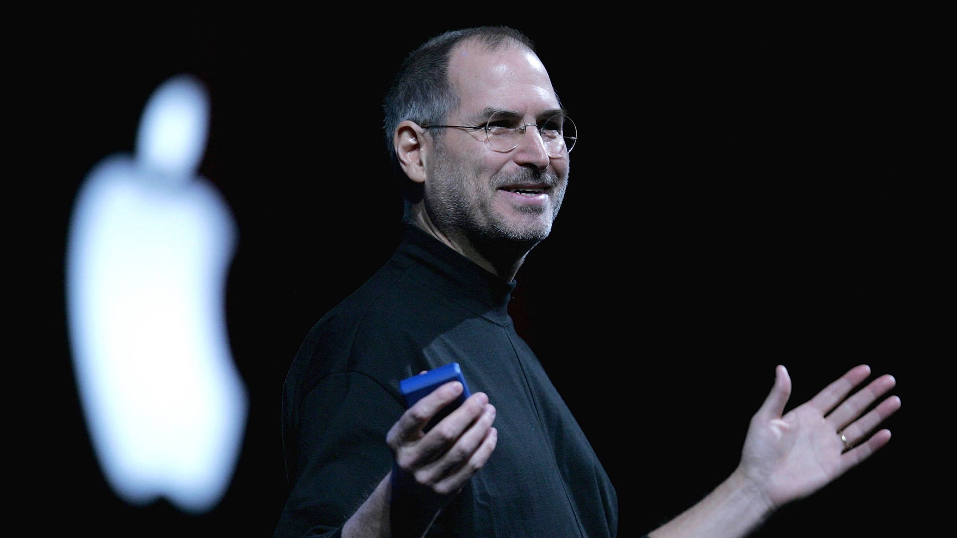 Steve Jobs 在舞台上進行演示，身後有發光的 Apple 標誌。