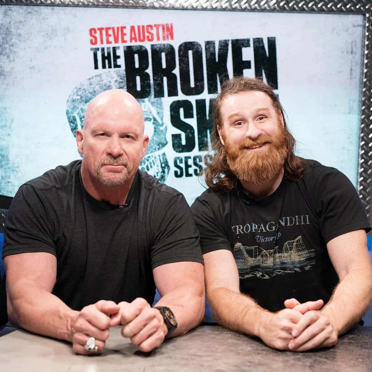 兩名男子坐在桌子前，背景為「Steve Austin The Broken Skull Sessions」。