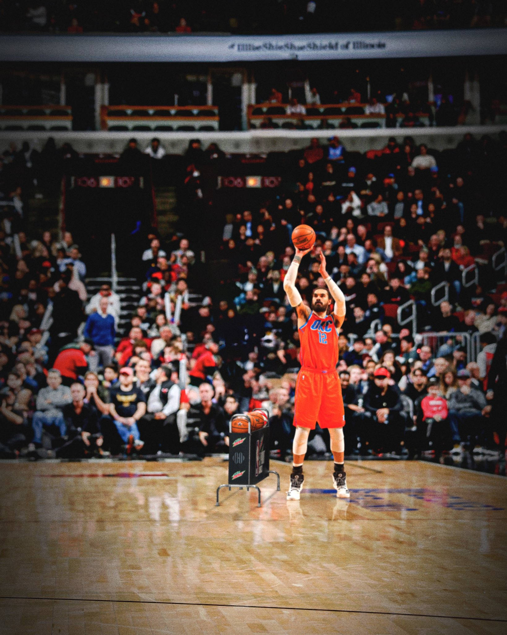 史蒂文·亞當斯OKC紅衣 壁紙 — 一名身穿橙色球衣的籃球運動員在明亮的場館燈光下，在全場觀眾專注注視中，投出一個罰球。