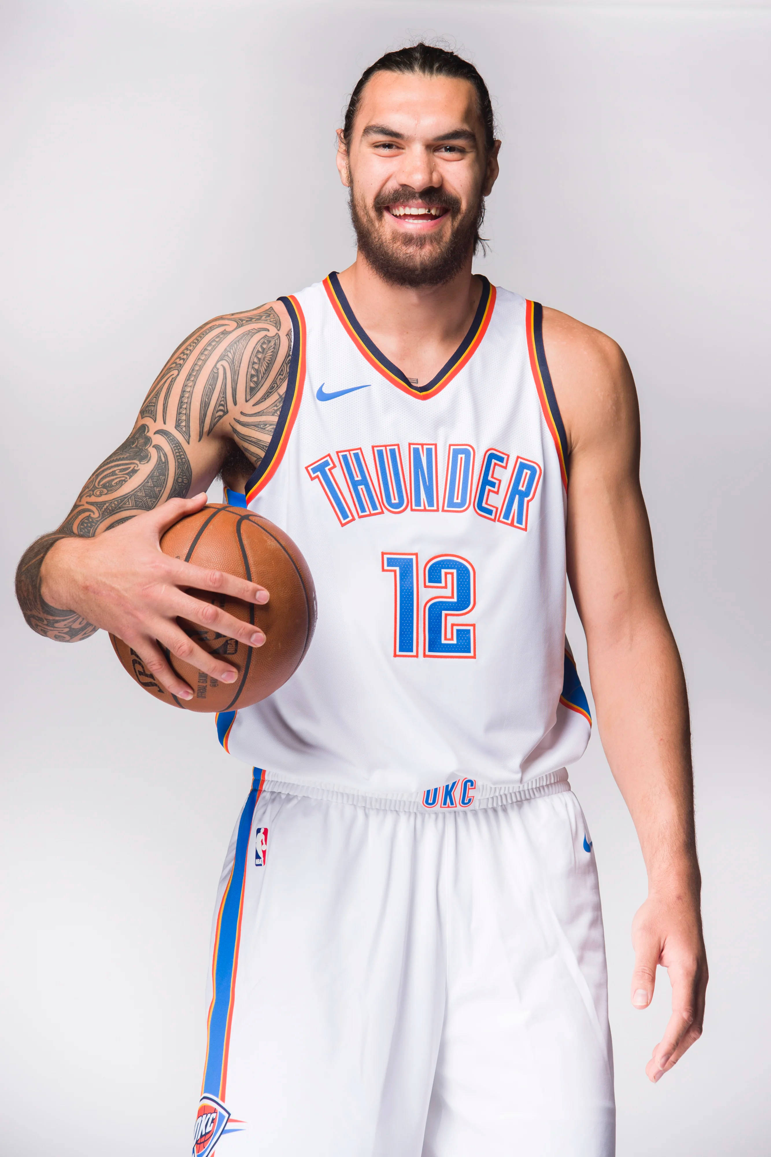 史蒂文·亞當斯OKC雷霆隊白色球衣 壁紙 — 一位微笑的籃球運動員身穿白色雷霆隊球衣，在純色工作室背景前持球。