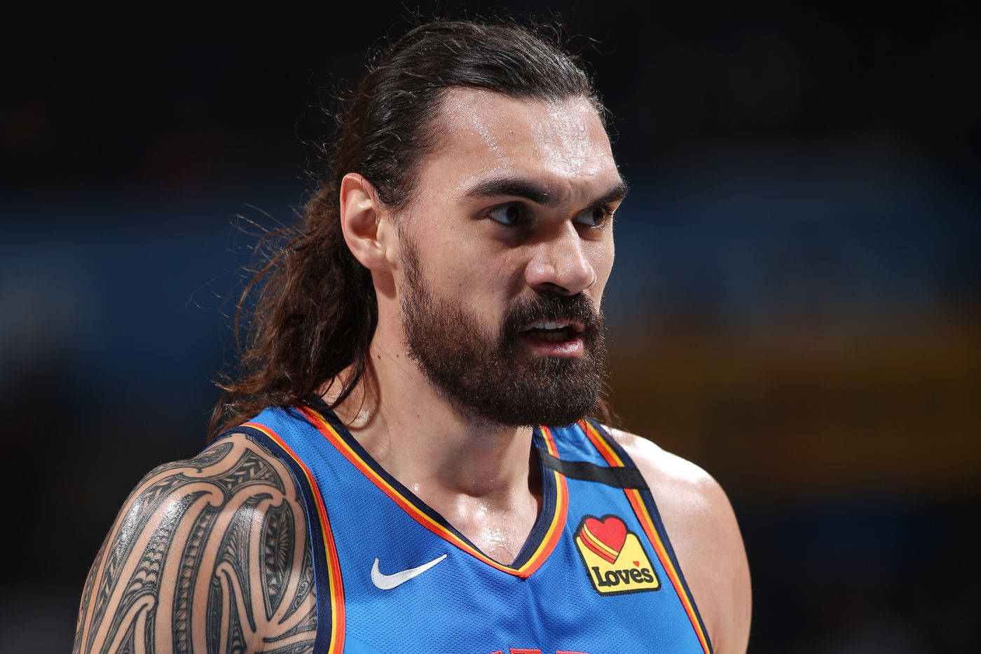 史蒂芬·亞當斯 OKC 雷霆隊 壁紙 — 專注的籃球運動員特寫，長黑髮、鬍鬚，身穿藍色球衣，手臂有紋身。
