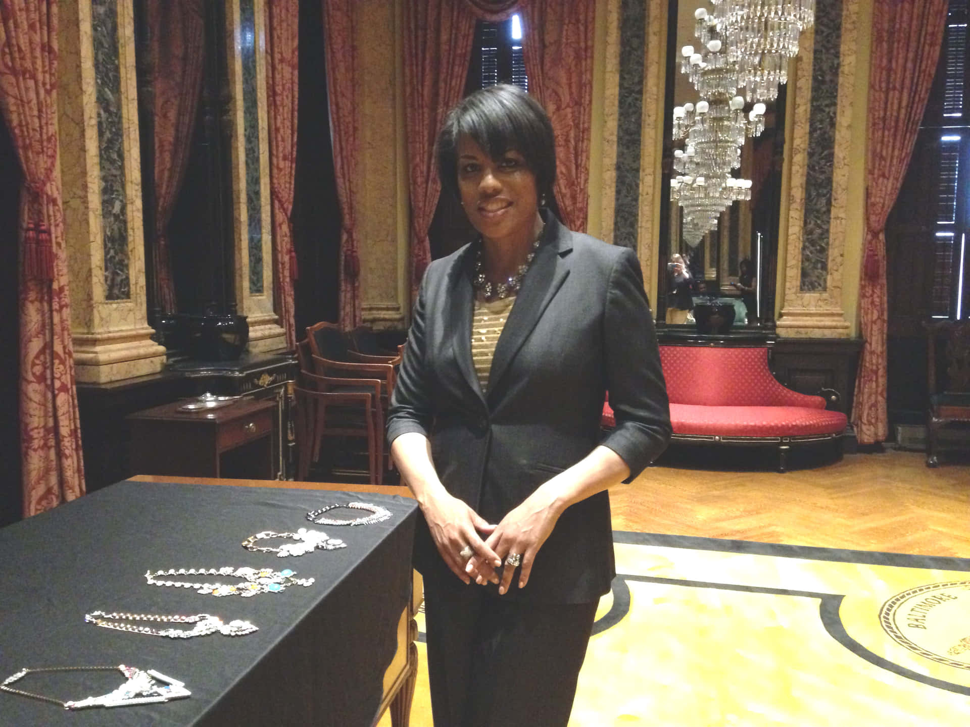 身穿黑色西裝的女子在富麗堂皇的房間內珠寶展示旁微笑。