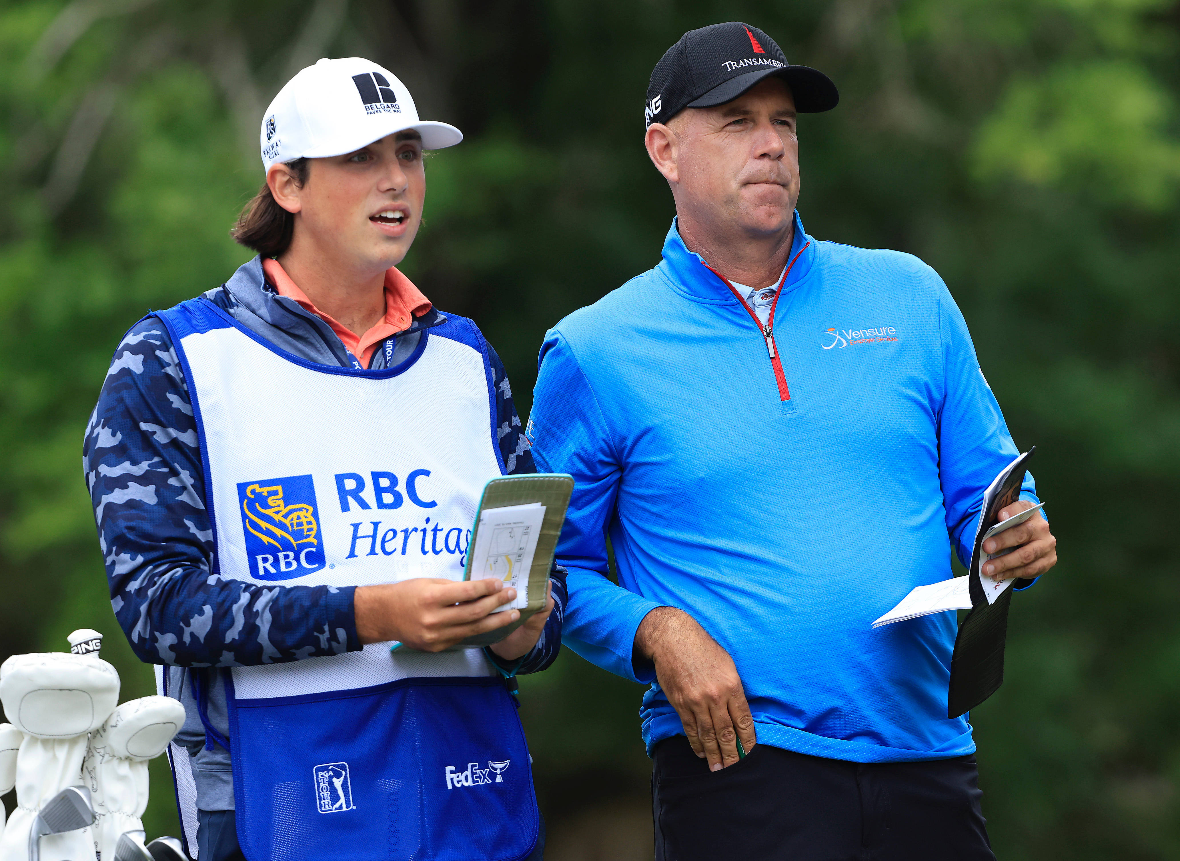 史都華·辛克與兒子同行 壁紙 — 兩名身穿藍色RBC Heritage裝備的高爾夫球手站在鬱鬱蔥蔥的綠色球場上，身後有樹木。