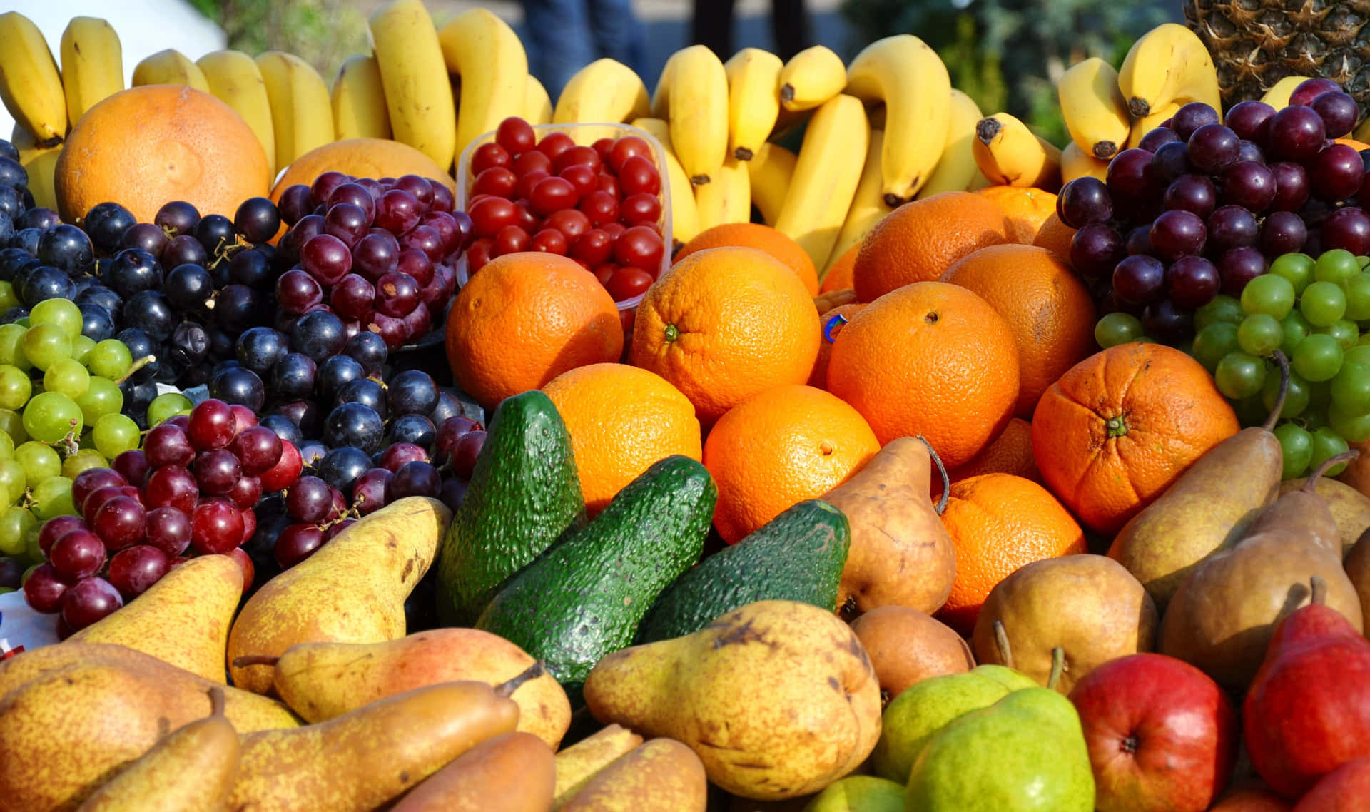 Winter Fruits 桌布 壁紙 — 各種新鮮水果包括香蕉、提子、橙、梨和牛油果，以色彩繽紛、豐富的堆疊方式排列的鮮豔特寫。