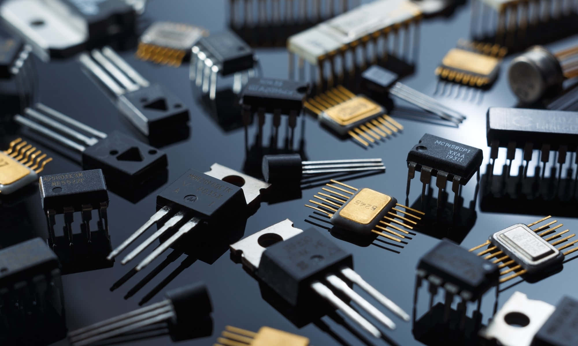 Electronic Components 桌布 壁紙 — 各種電子元件（如晶體管和集成電路）散落在反光黑色表面上的特寫。