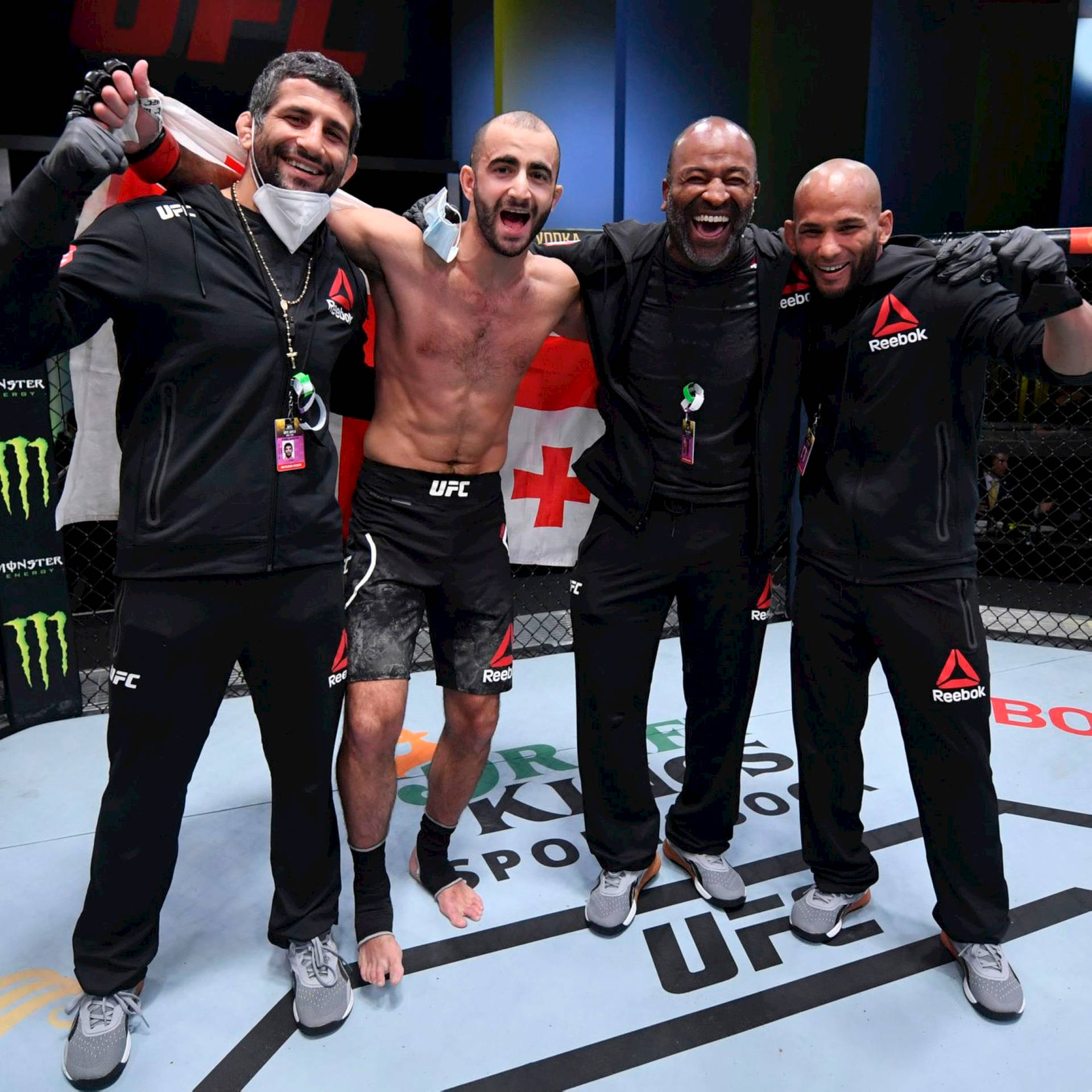 四名UFC拳手和工作人員在八角籠中互相擁抱慶祝勝利。