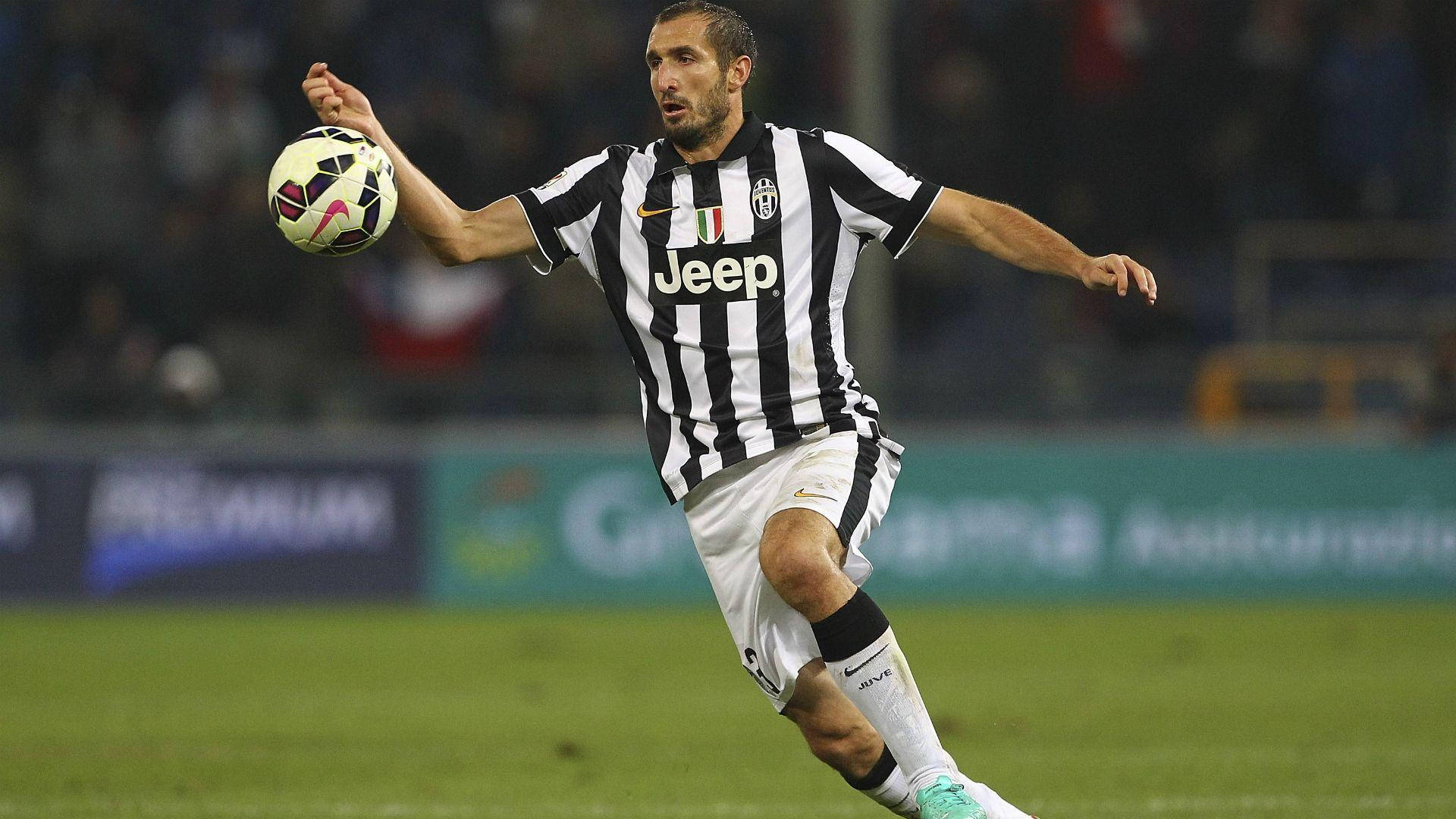 吉奧吉歐·基耶利尼 足球賽強力射門 壁紙 — 一位身穿黑白間條球衣的祖雲達斯足球員在球場燈光下，於綠色草地上控球前進。