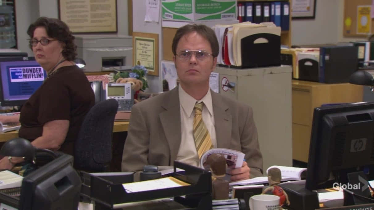 Dwight Schrute 在 Dunder Mifflin 辦公室拿著雜誌，眼神專注。