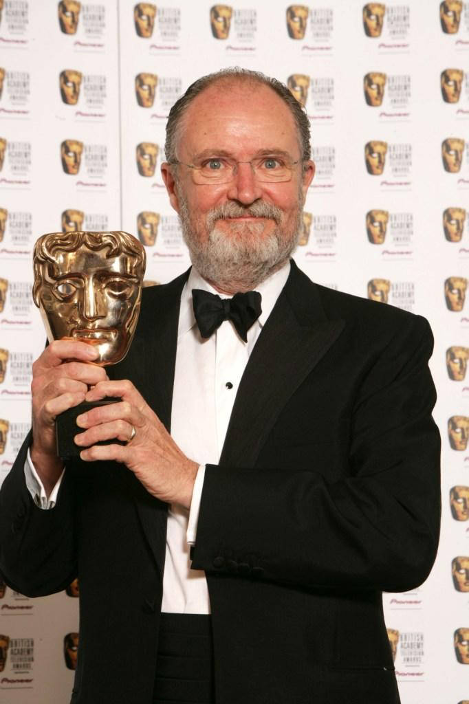 吉姆·布勞德本特獲BAFTA最佳男配角獎 壁紙 — 一位留鬍鬚、身穿禮服的男士，在品牌背景前微笑著手持金色BAFTA獎座。