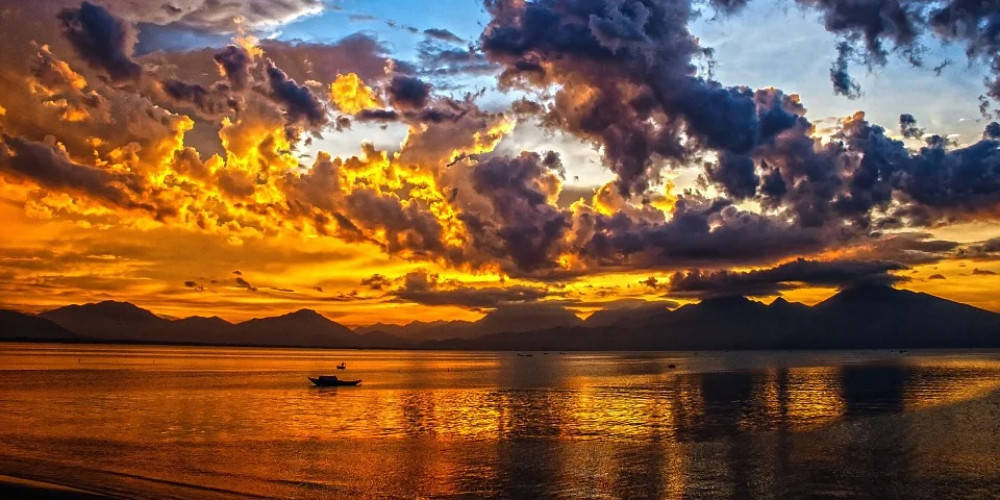 一艘小船在寧靜的水面上休息，下方是充滿活力的夕陽天空，遠方有山巒。