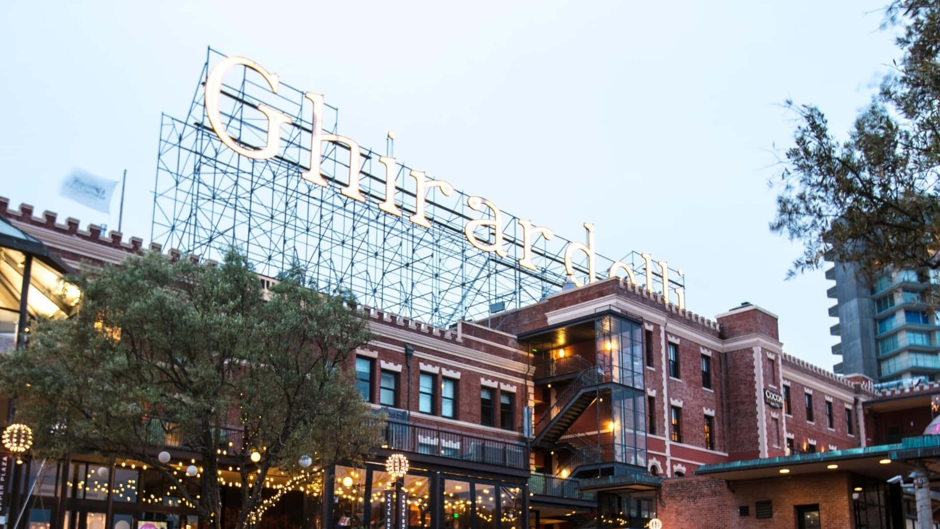黃昏時分的 Ghirardelli 建築，帶有發光標誌和燈串。
