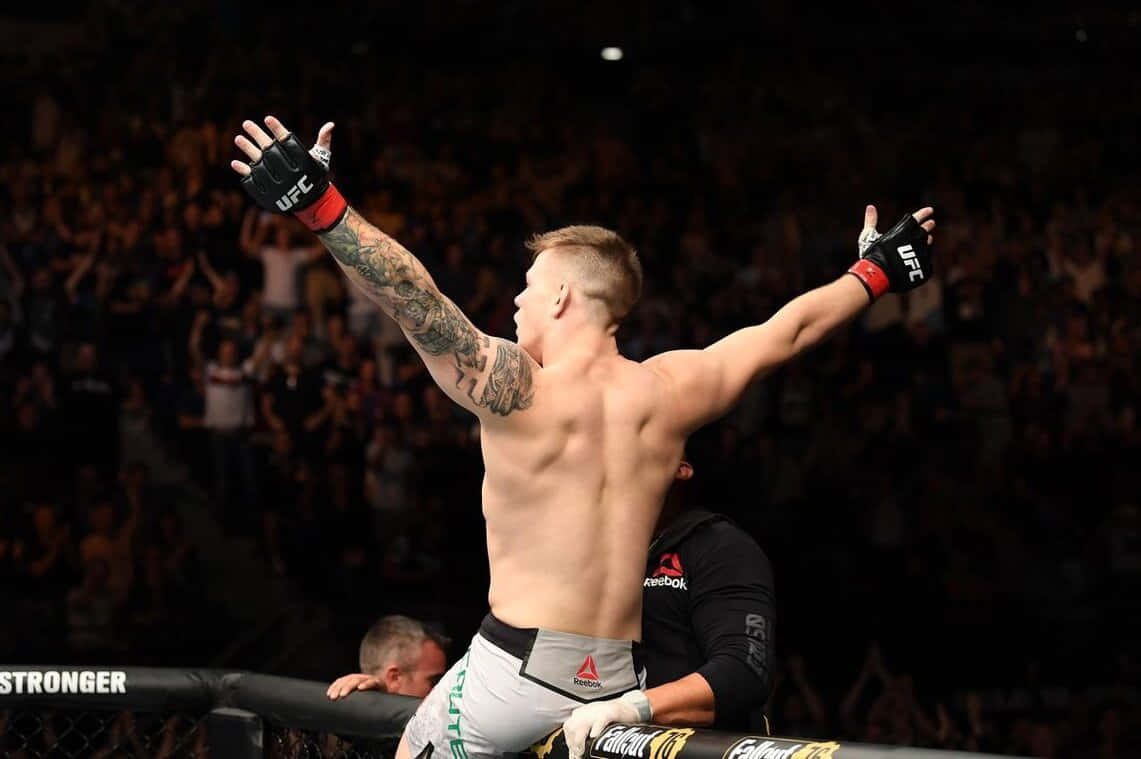MMA拳手在八角籠中高舉雙臂慶祝勝利。