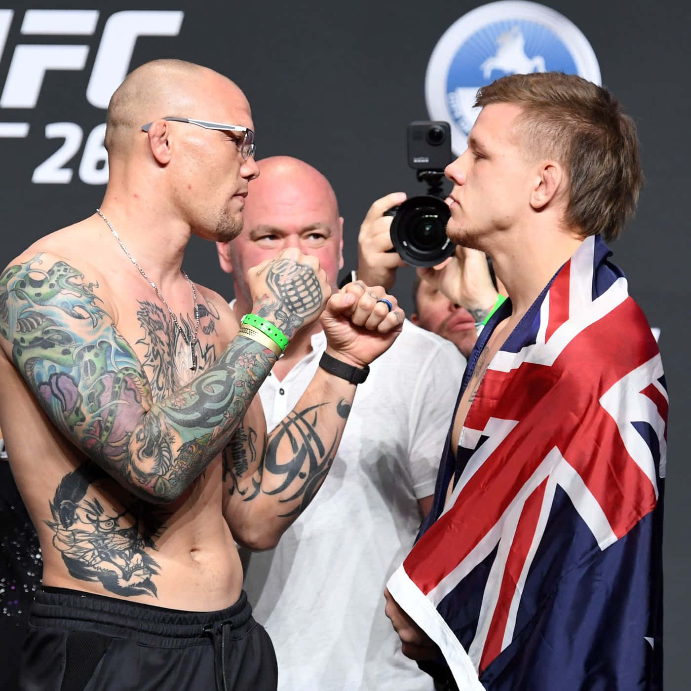 兩位男性UFC拳手在比賽前互相凝視，一人有紋身，另一人披著英國國旗。