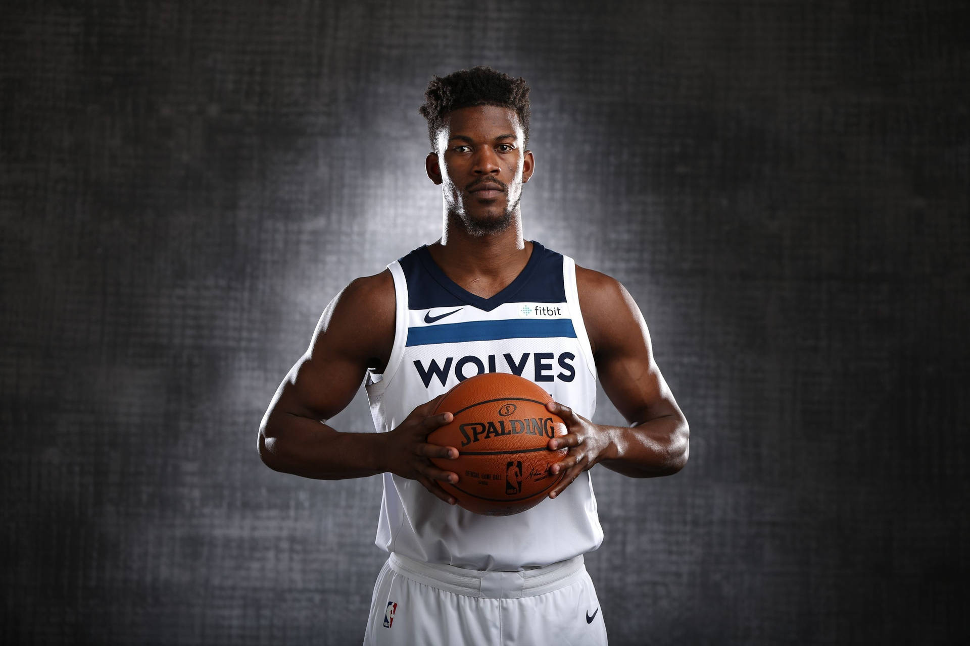職業籃球運動員身穿狼隊球衣，在深色背景前拿著一個 Spalding 籃球。