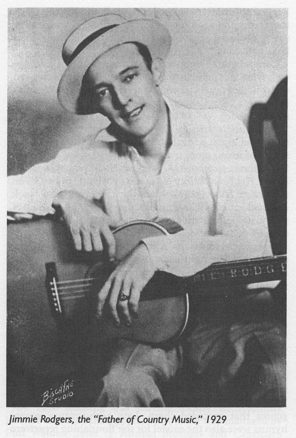 吉米·羅傑斯傳記肖像 壁紙 — 一張復古黑白肖像，Jimmie Rodgers 在錄音室環境中微笑著抱著一把原聲結他。