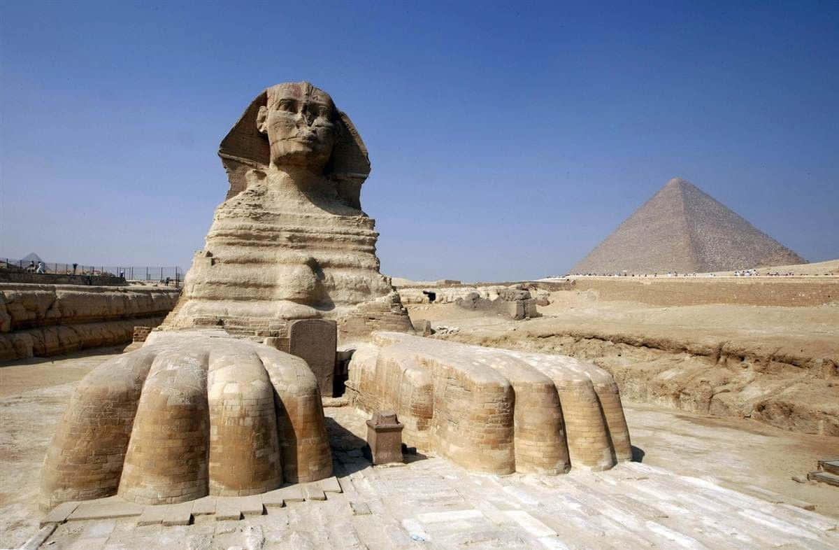 Egypt 桌布 壁紙 — 吉薩大獅身人面像在沙漠中雄偉地矗立，背景中可看到卡夫拉金字塔，天空清澈湛藍。