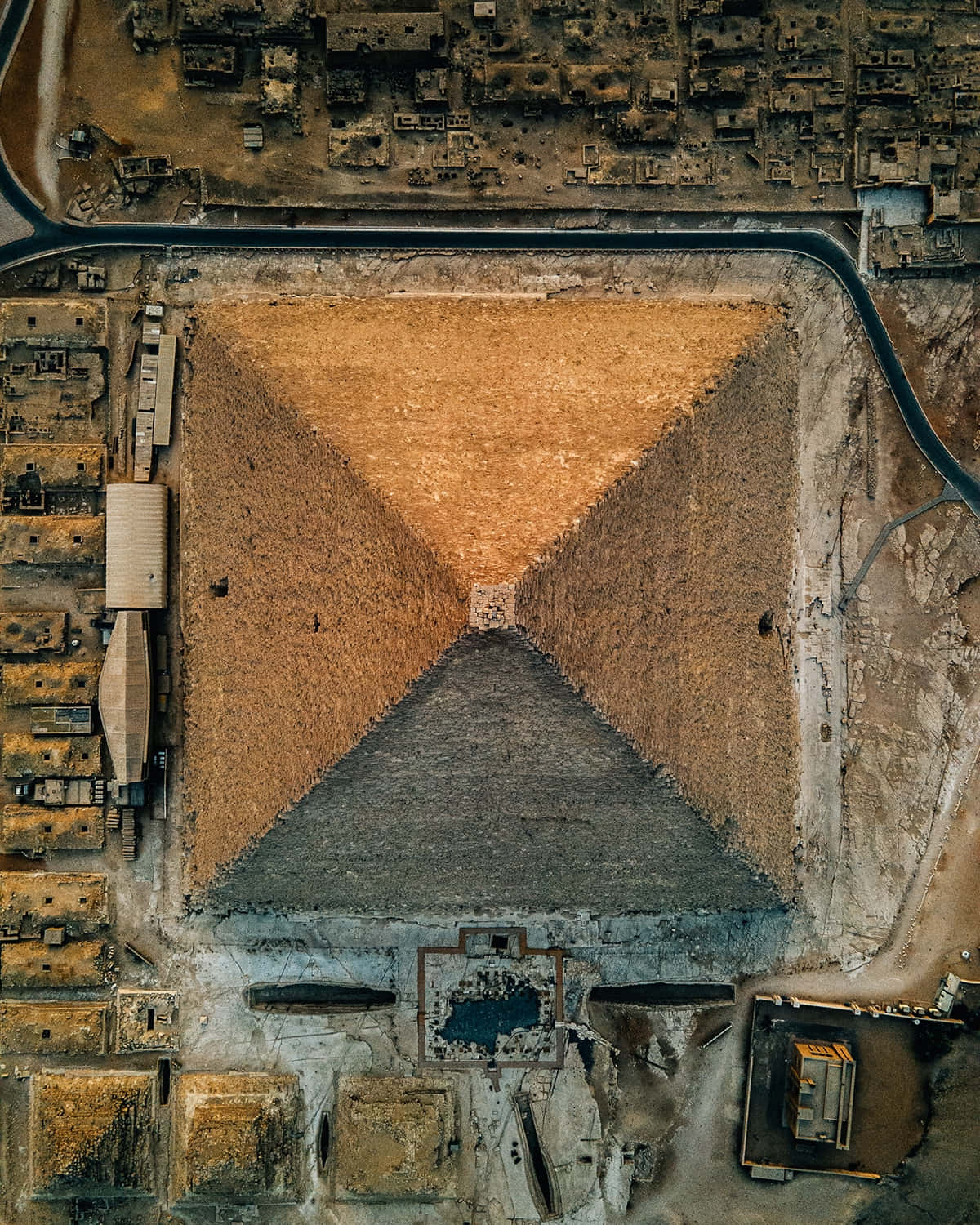 從高空俯瞰一座古老金字塔，周圍是沙漠廢墟和現代道路。