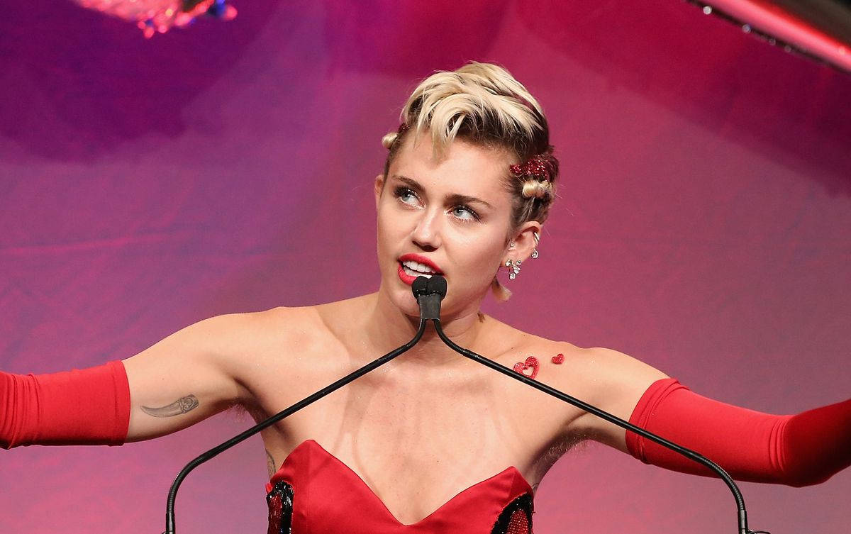 Miley Cyrus 在舞台上穿著紅色服裝，雙臂張開表演。