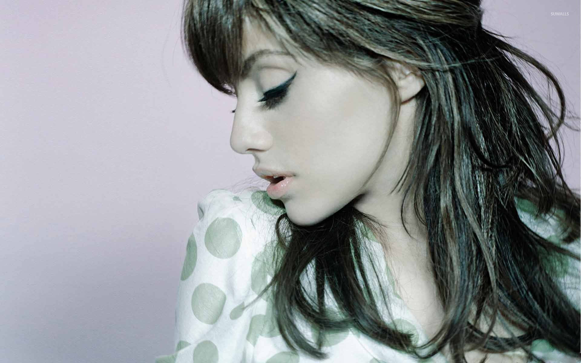 深色頭髮、畫著大膽眼線的女性，在薰衣草背景下穿著波點襯衫向下看。