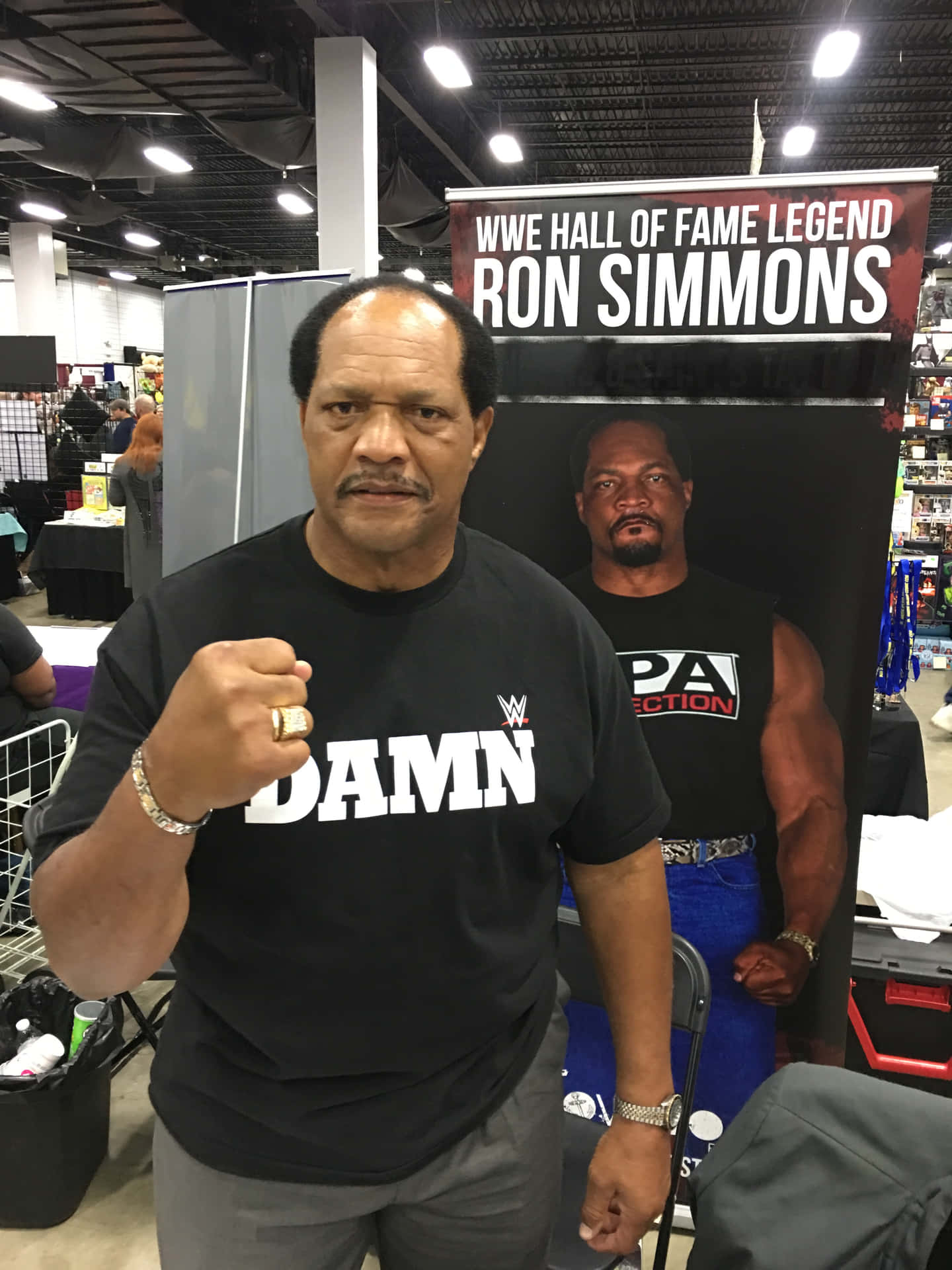 WWE名人堂成員Ron Simmons在會議上穿著印有'DAMN'的黑色T恤和戒指擺姿勢。