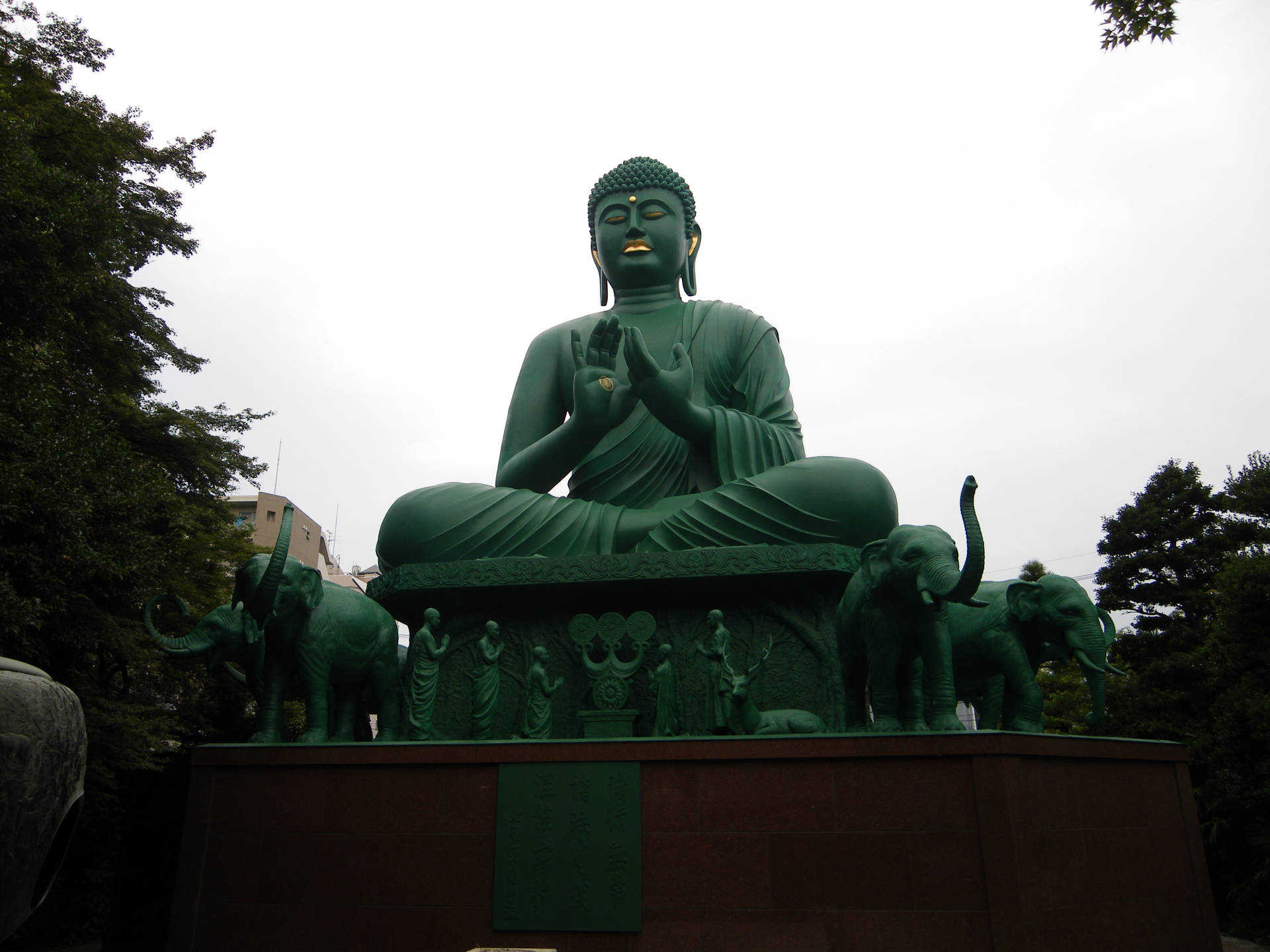 公園環境中，被大象環繞的大型綠色佛像。