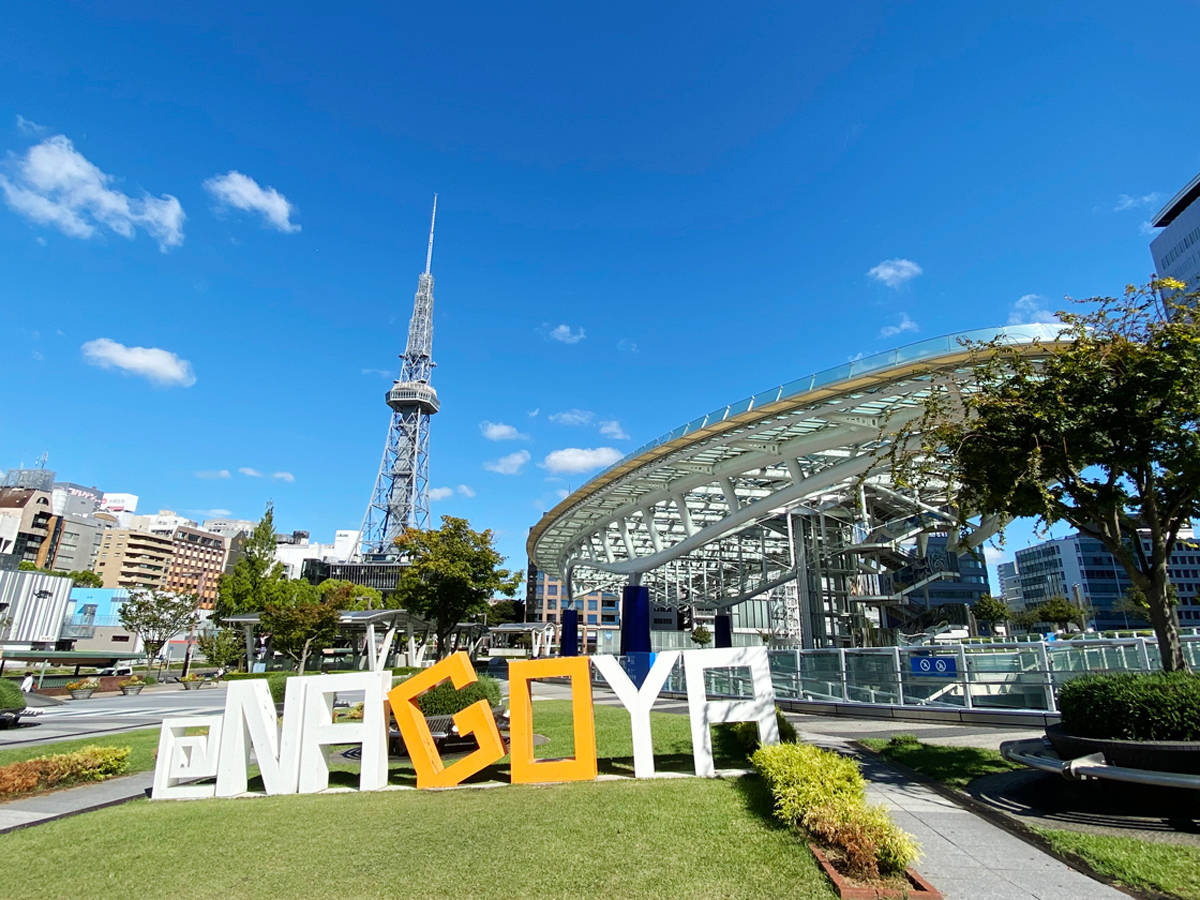 名古屋大通公園地標 壁紙 — 大型彩色NAGOYA字母放置在草地上，背景是明亮的藍天、散落的雲朵和名古屋電視塔。