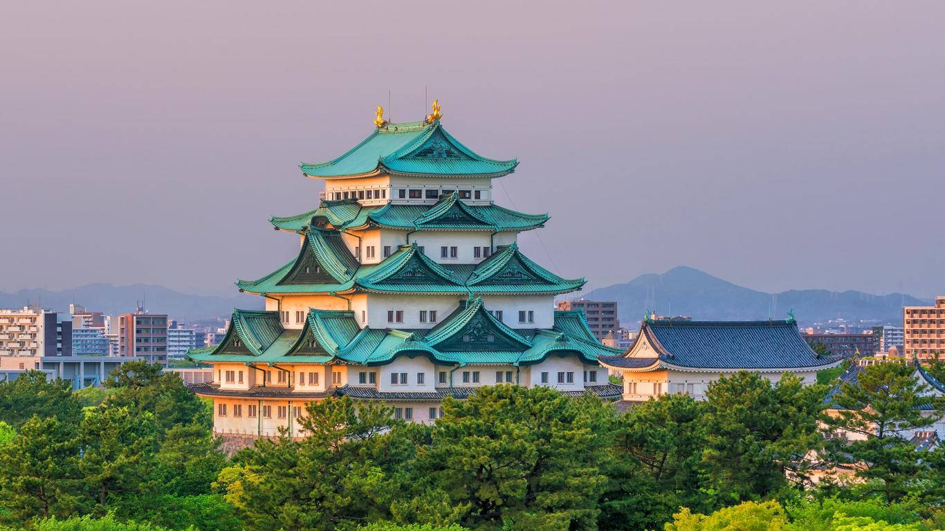 名古屋大須城 壁紙 — 一座雄偉的日本城堡，擁有綠色瓦片屋頂，在柔和的紫色暮色天空中，聳立在茂密的樹木之上。