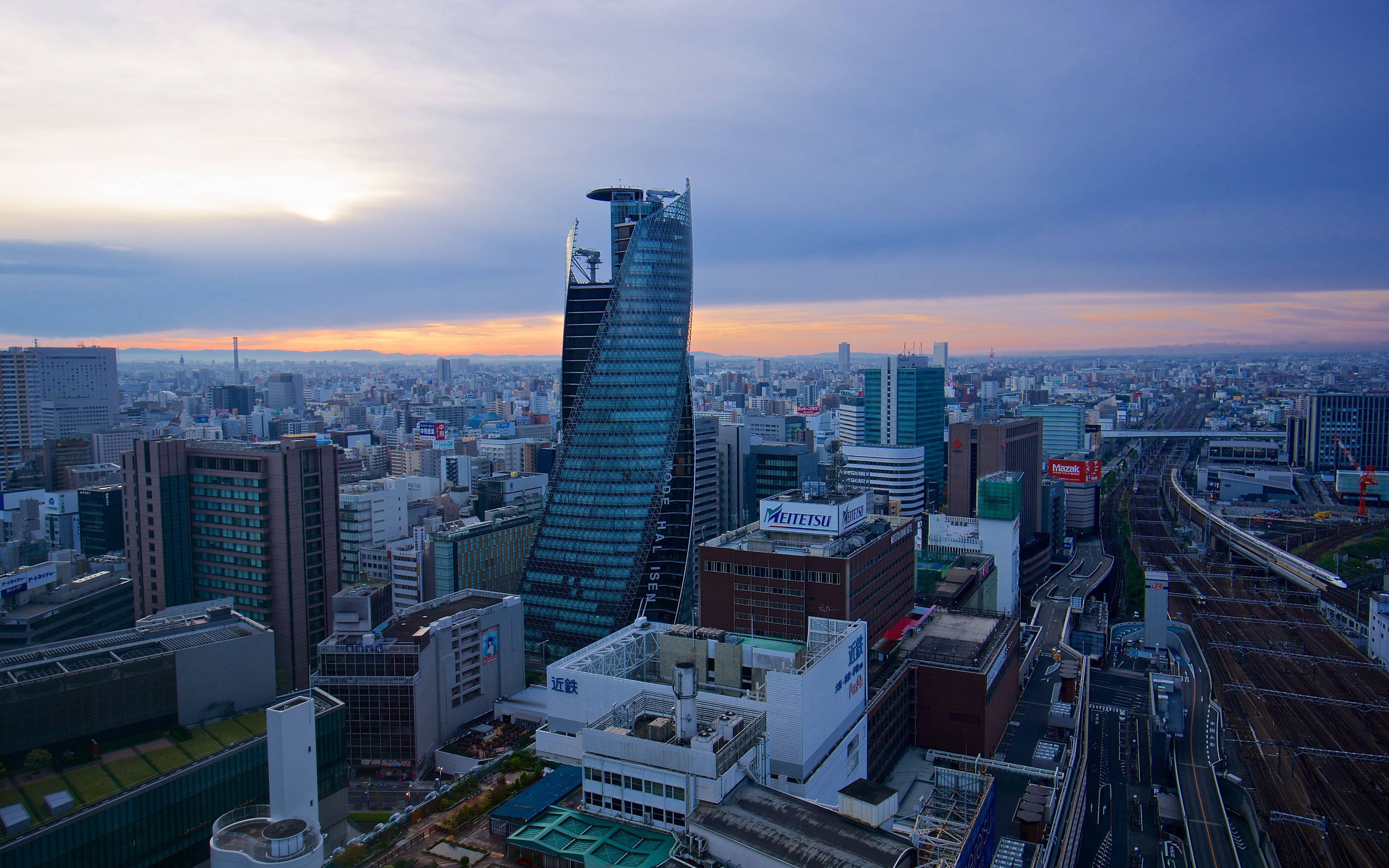 名古屋市景 壁紙 — 黃昏時分廣闊城市景觀的鳥瞰圖，一座獨特的彎曲摩天大樓在漸變天空下主導天際線。