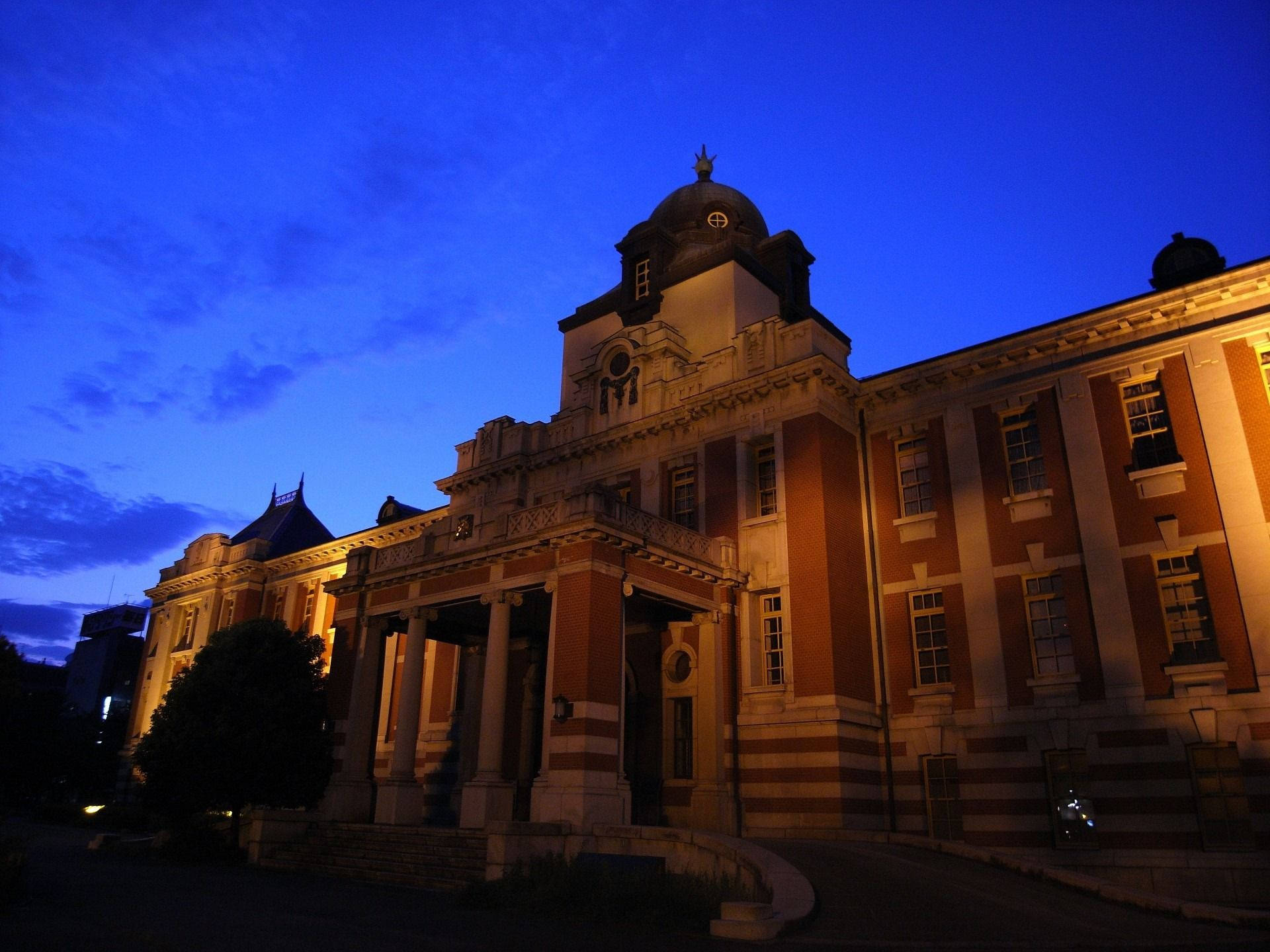 名古屋市立圖書館夕照 壁紙 — 一座宏偉的歷史建築，溫暖的燈光在深藍色的暮色天空中閃耀。