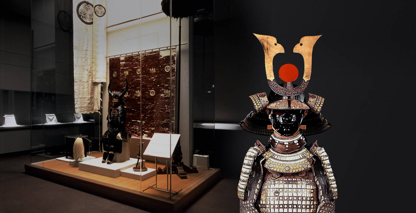 名古屋德川博物館展覽 壁紙 — 一件帶有紅色太陽徽章的詳細武士鎧甲，在燈光昏暗的博物館畫廊中，矗立在玻璃展示櫃旁，格外引人注目。