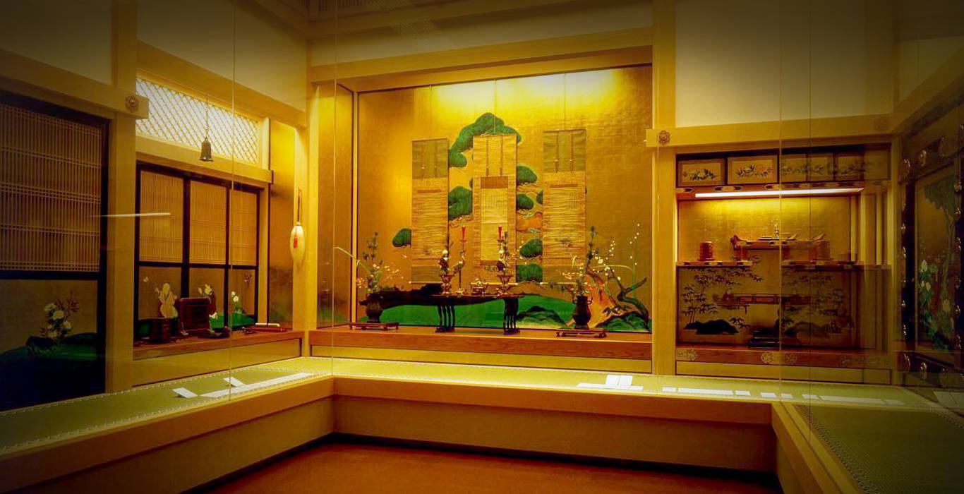 名古屋德川美術館 壁紙 — 溫暖照明的傳統日本博物館展覽，展示金色屏風、花卉佈置及玻璃櫃下的漆器工藝品。