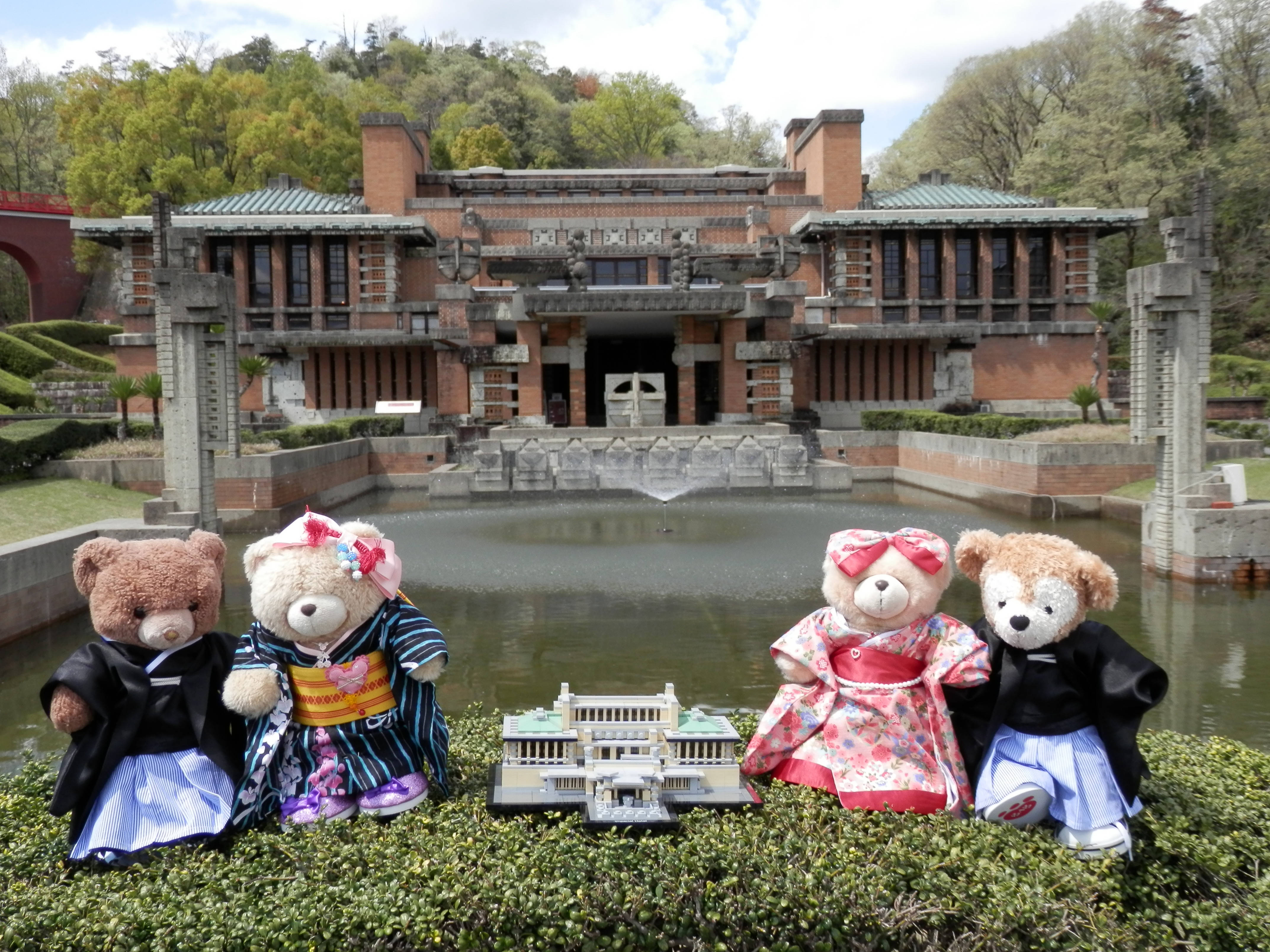 名古屋明治村博物館小熊 壁紙 — 四隻穿著色彩繽紛和服的泰迪熊坐在草地上，面前是一座倒映在水中的宏偉日本建築的微型複製品。