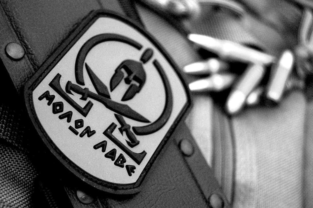 戰術裝備上 Molon Labe 布章的特寫，背景有子彈。