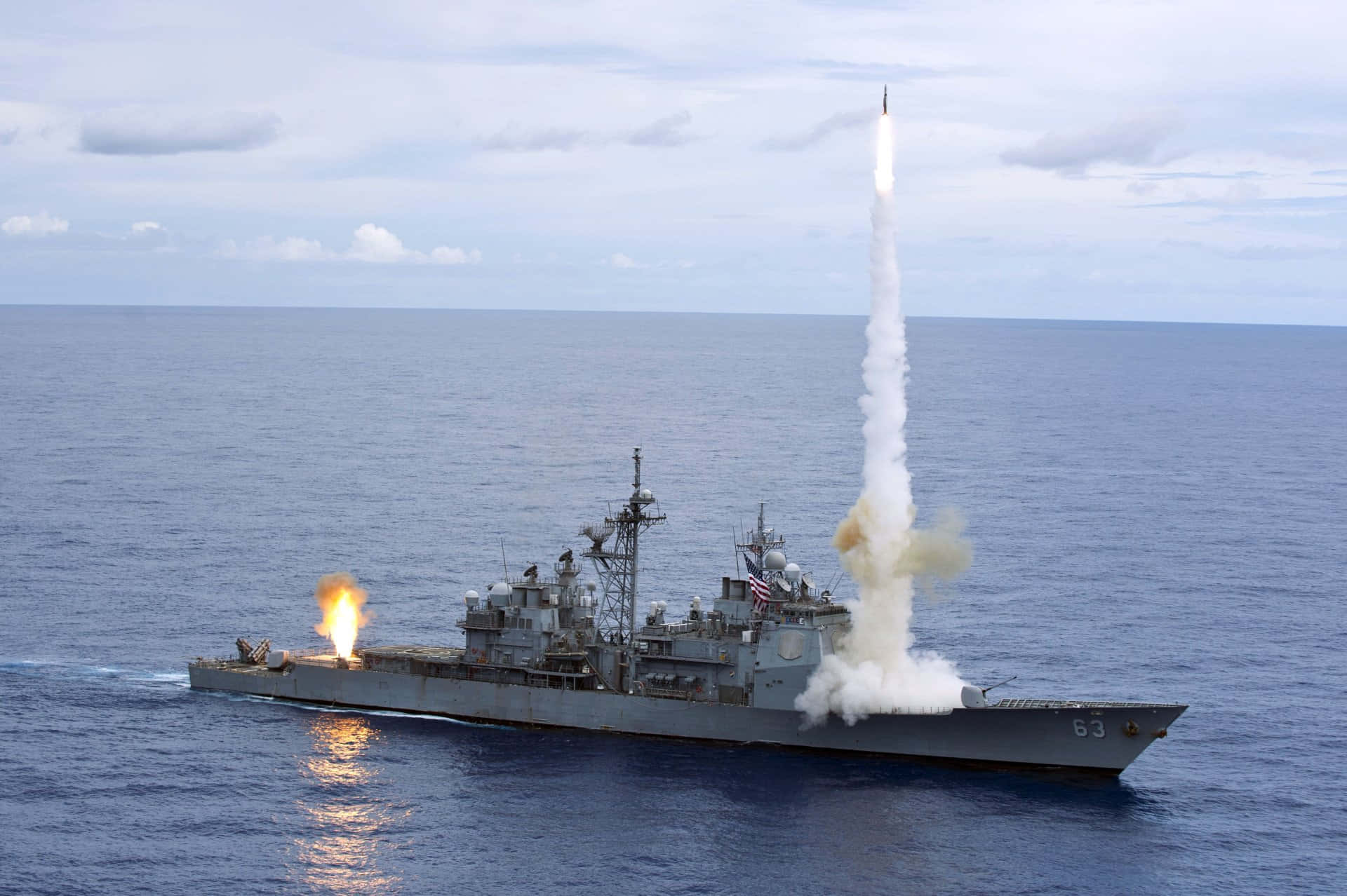 向勇敢的海軍官兵致敬 壁紙 — 一艘灰色軍艦在海洋上空發射導彈，明亮的火焰和煙霧在陰雲密佈的天空中拖曳。