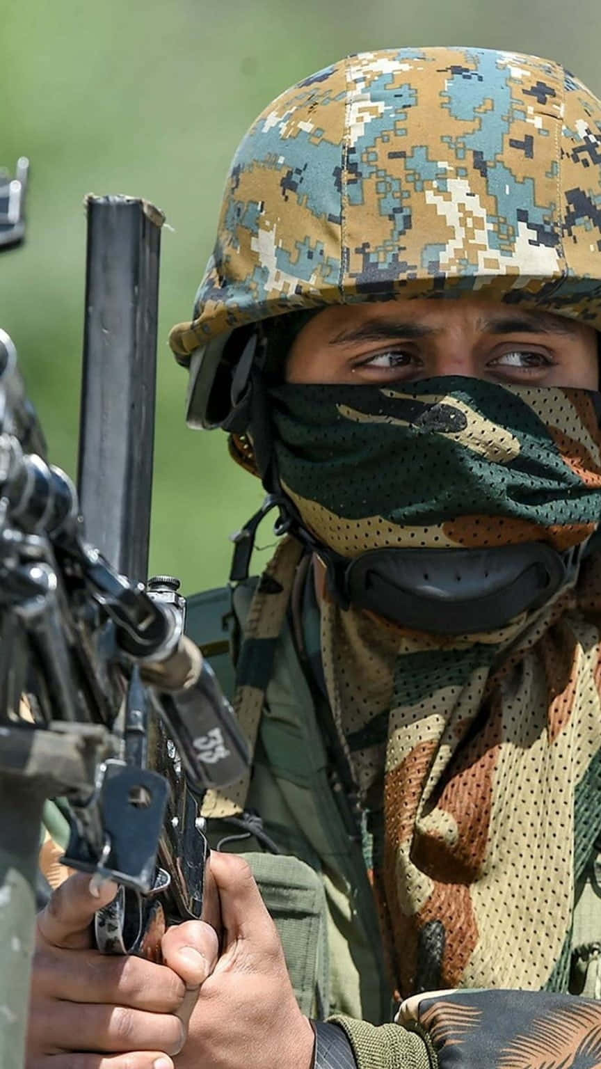 向印度陸軍英勇士兵致敬 壁紙 — 一名身穿迷彩裝備和面罩的士兵，在模糊的綠色背景下，專注地握著步槍。