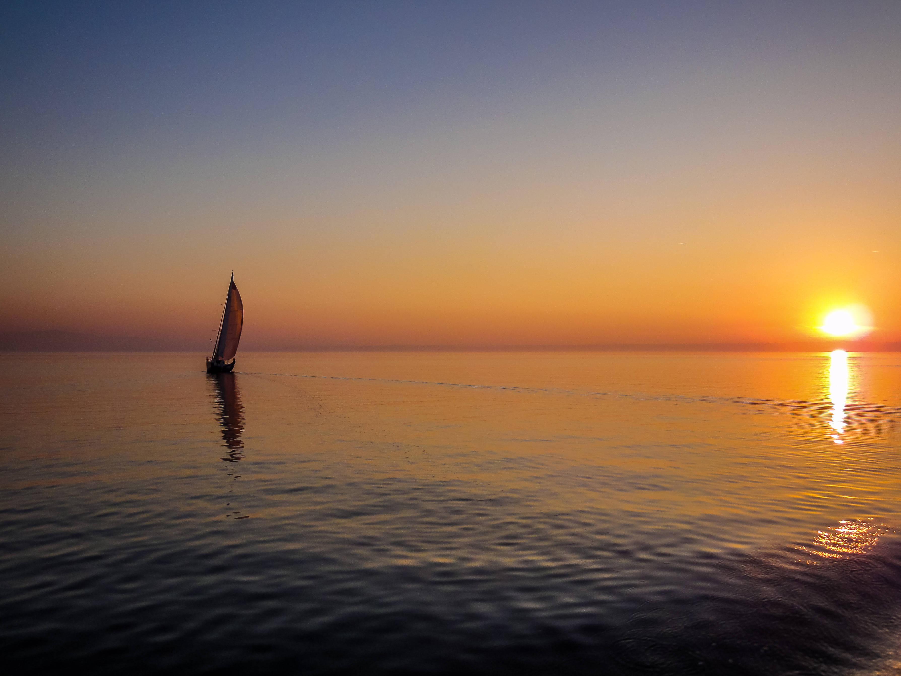向右航行 壁紙 — 一艘孤獨的帆船在平靜的水面上滑行，夕陽以橙色和藍色的漸變落下。