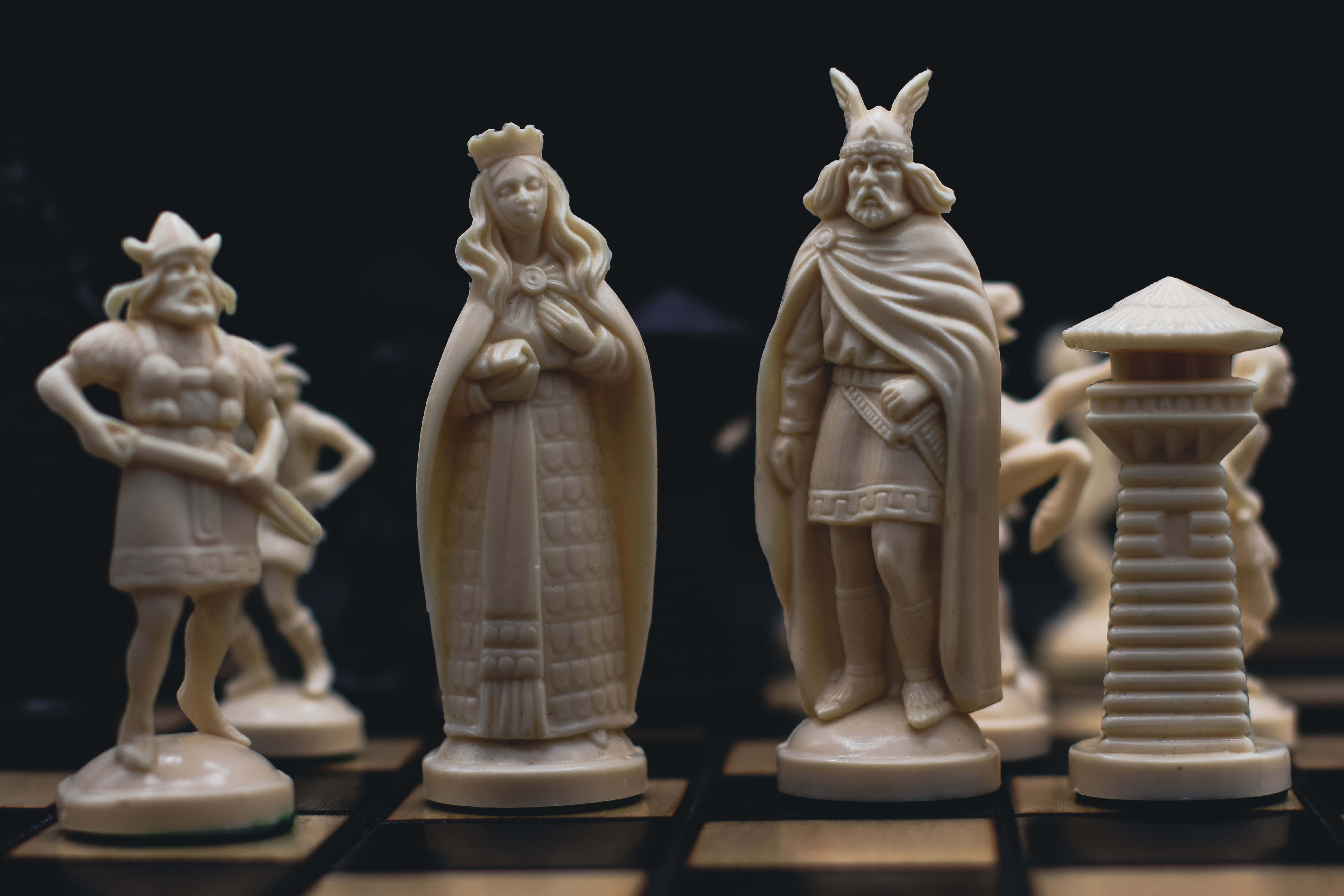 君王統治一切 壁紙 — 優雅的象牙色國際象棋棋子，中世紀戰士女王和國王站在深色棋盤上。
