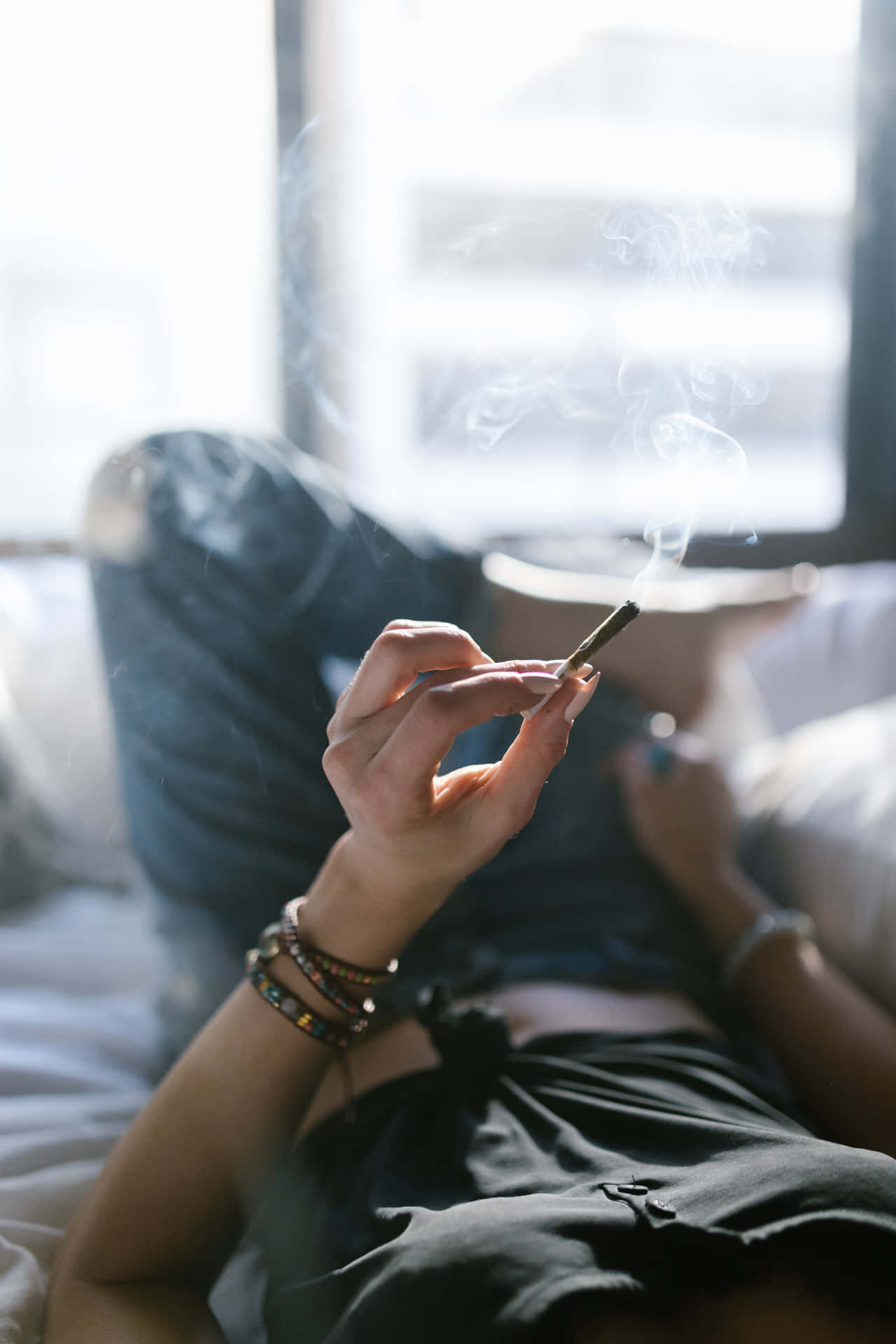 人躺在床上手持點燃香煙，煙霧在窗邊上升