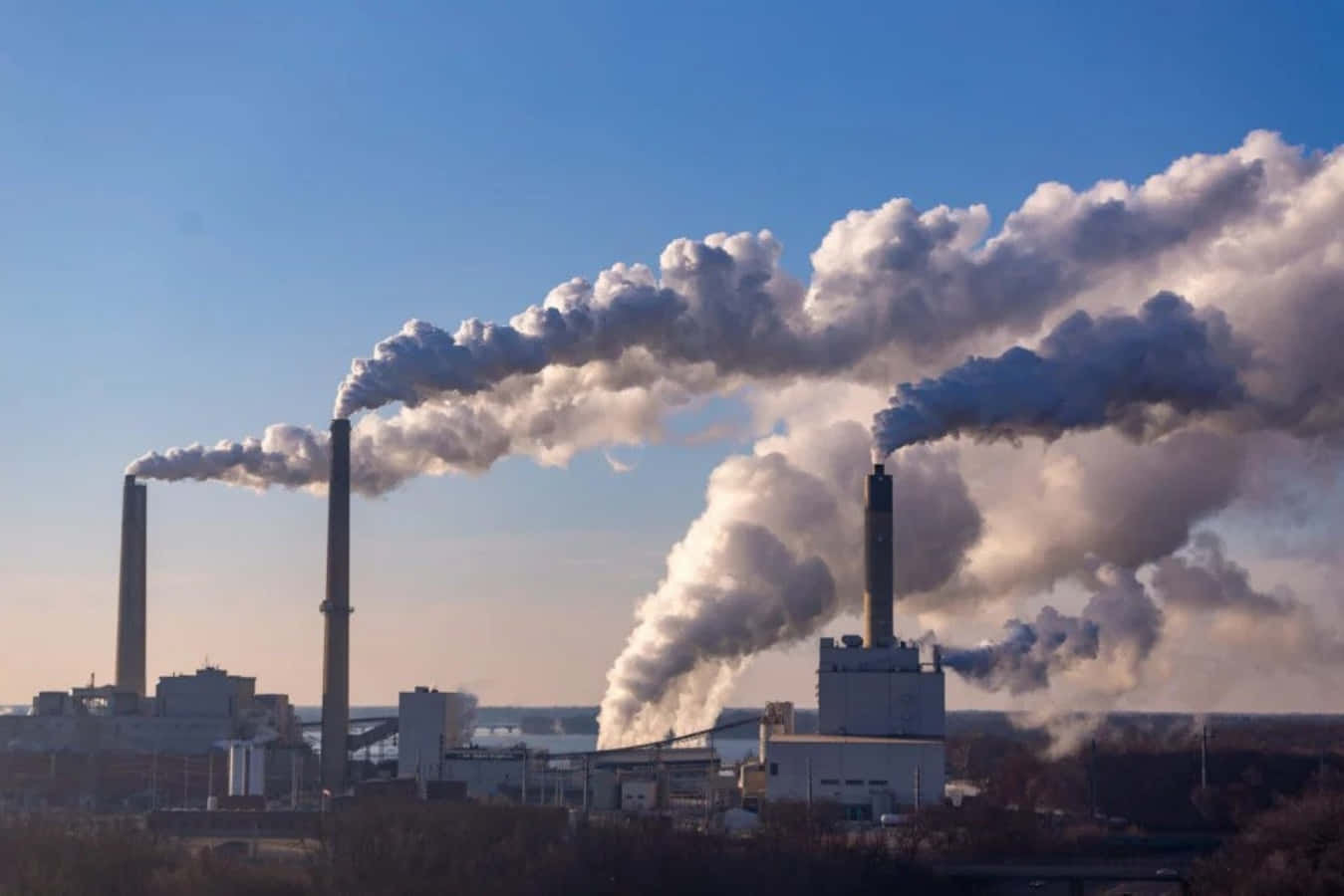 吸入受污染空氣是健康威脅 壁紙 — 工業發電廠的煙囪在日出時向晴朗的藍天噴出濃厚的灰色煙霧。