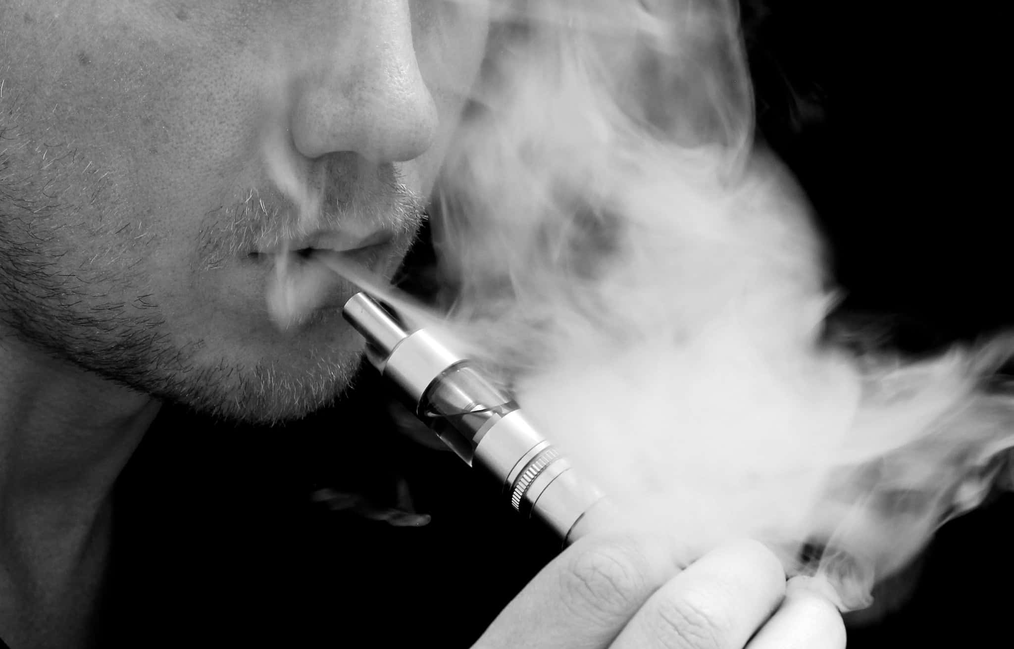 吸煙的滿足感 壁紙 — 特寫黑白照片，一名男子在黑暗背景下呼出電子煙的濃厚煙霧。
