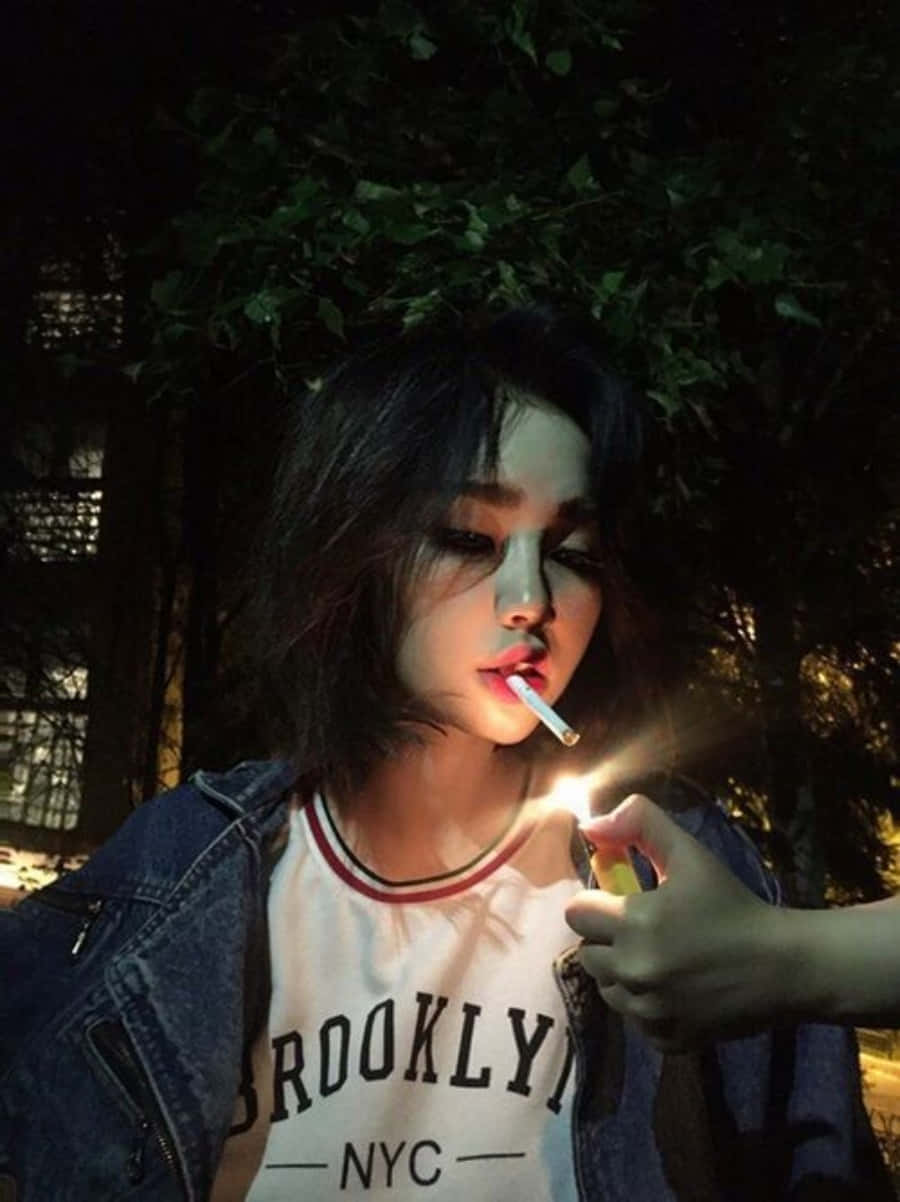 年輕女性在戶外夜晚穿著牛仔外套點燃香煙。