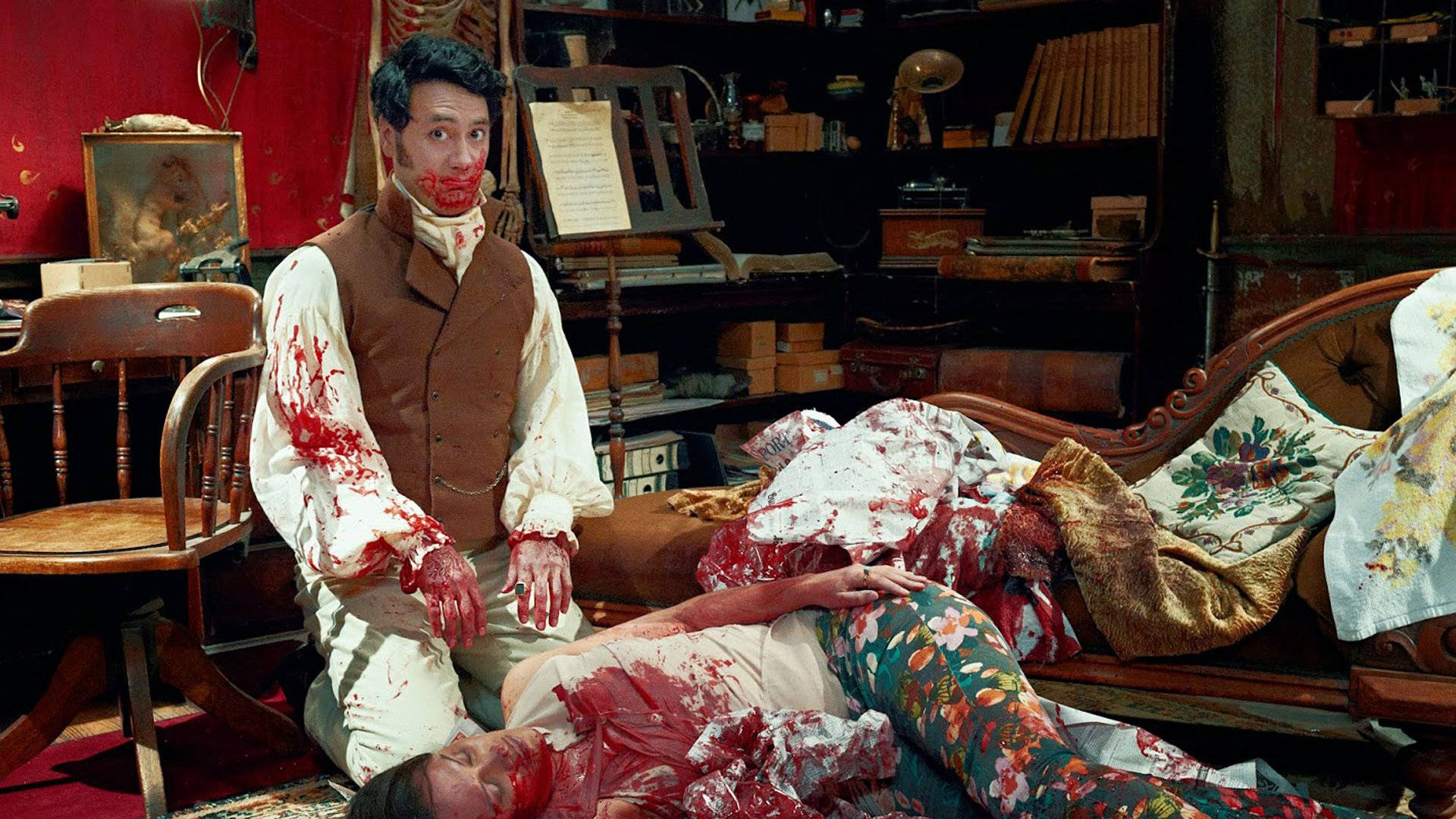 《吸血鬼生活》血腥女子 壁紙 — 一個穿著復古服裝、渾身是血的男人，跪在一個同樣渾身是血的女人旁邊，女人躺在一張花卉圖案的沙發上，房間雜亂且燈光昏暗。