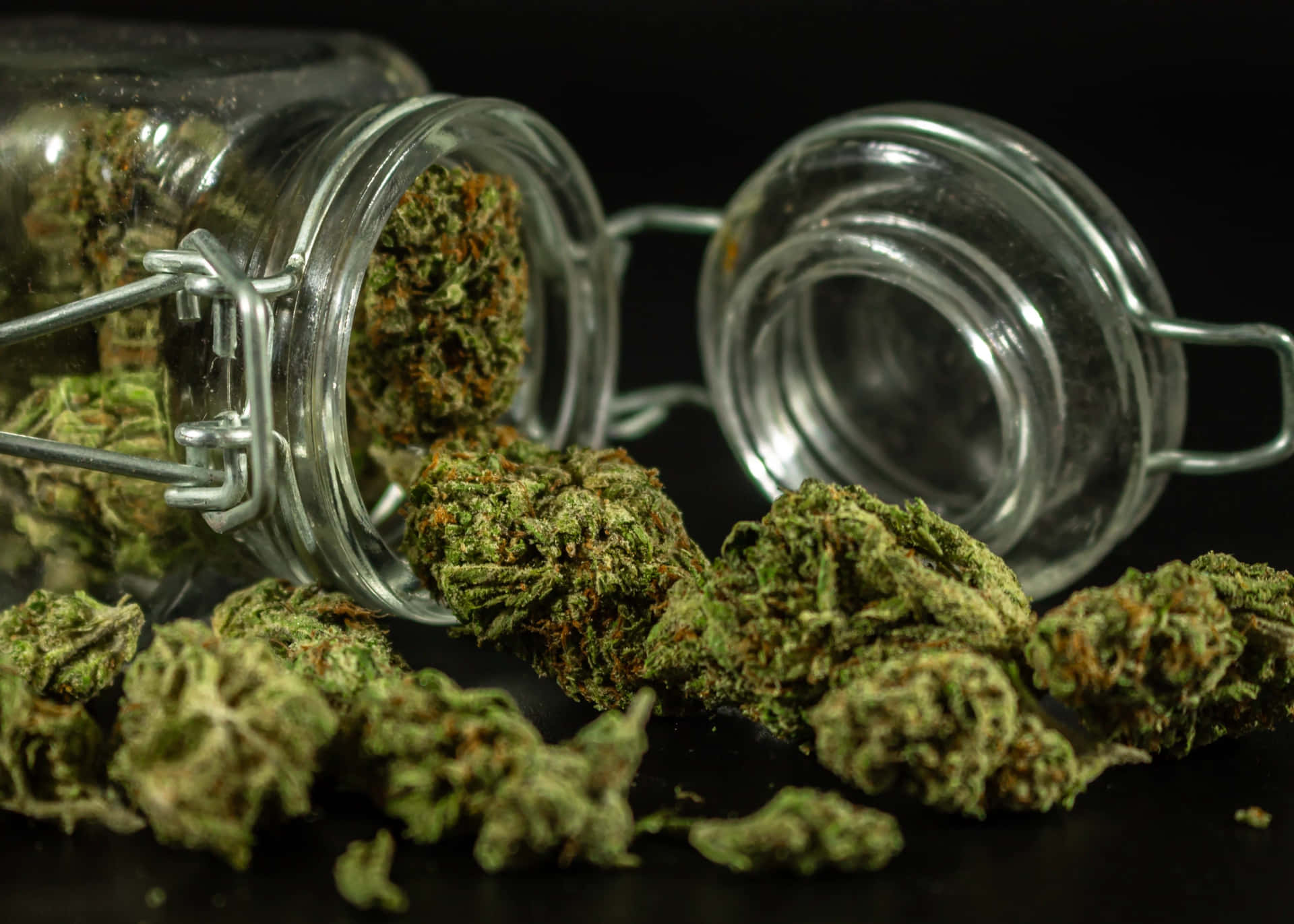 乾燥大麻花蕾從玻璃罐中灑出在黑色表面上。
