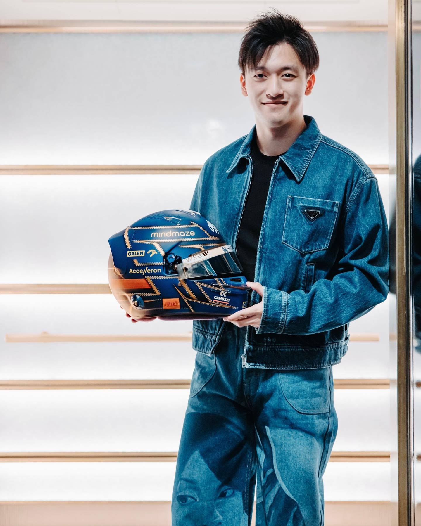 年輕男子身穿牛仔布，在攝影棚內手持賽車頭盔。