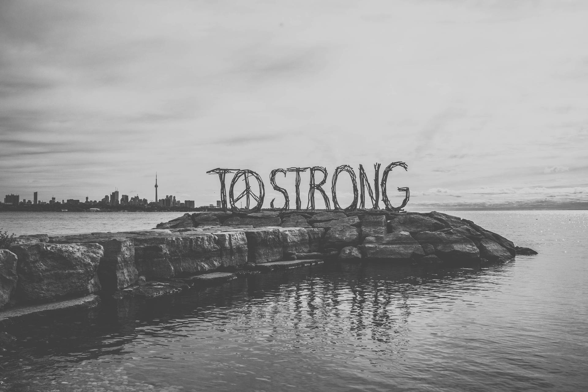 岩石島上「TO STRONG」編織標誌，背景為城市天際線。