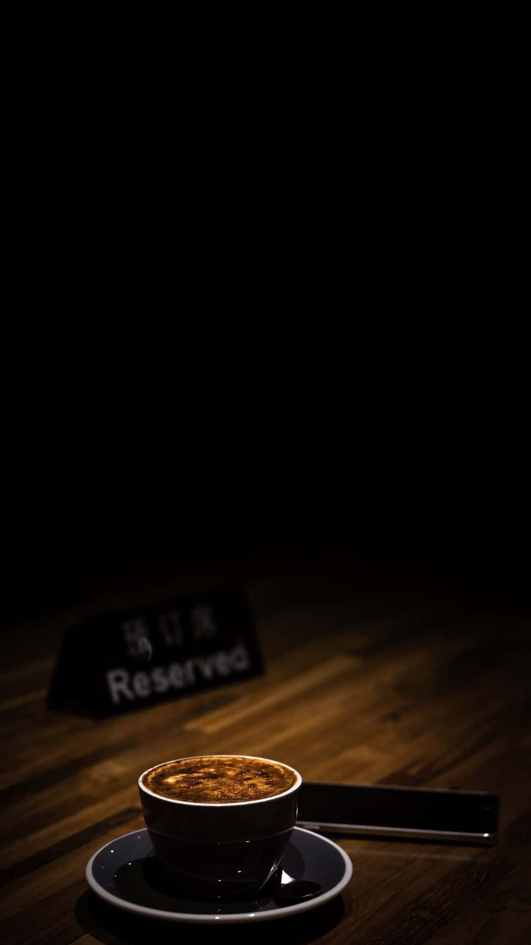 木桌上碟子裡的一杯濃縮咖啡，旁邊有電話和已預訂的牌子。