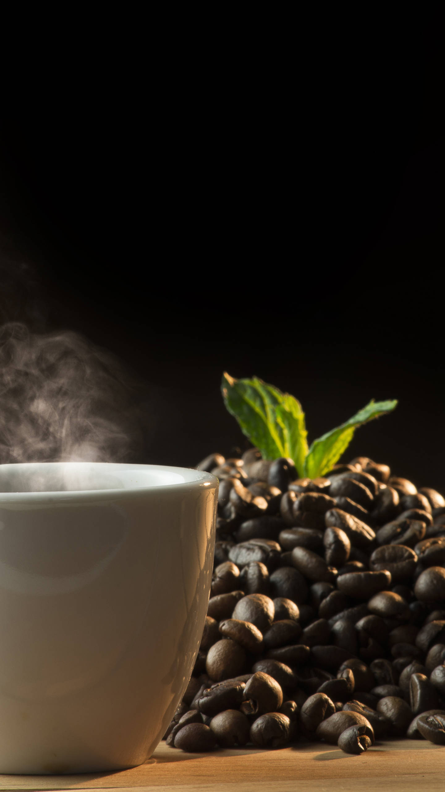 咖啡杯與咖啡豆 壁紙 — 一杯冒煙的白色咖啡杯，旁邊有一堆烘焙過的咖啡豆和新鮮薄荷葉，背景深色。