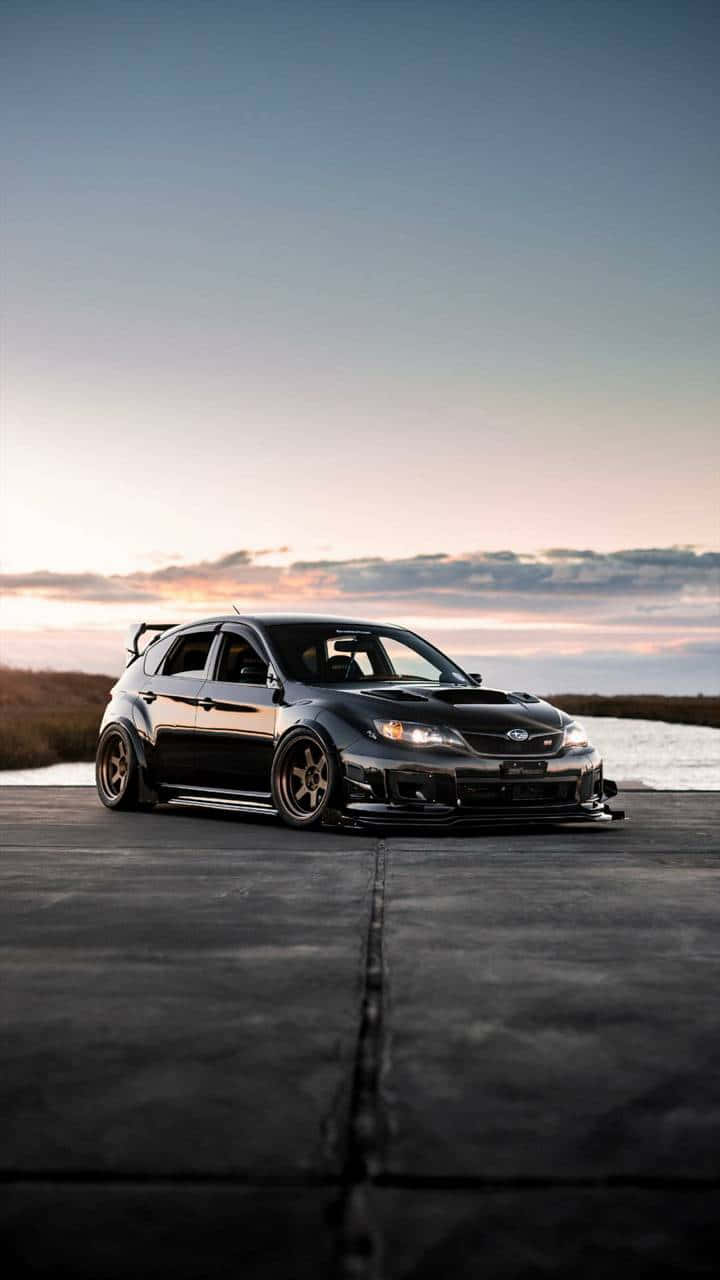 黑色改裝Subaru WRX STI在日落時停放在水邊的混凝土上。
